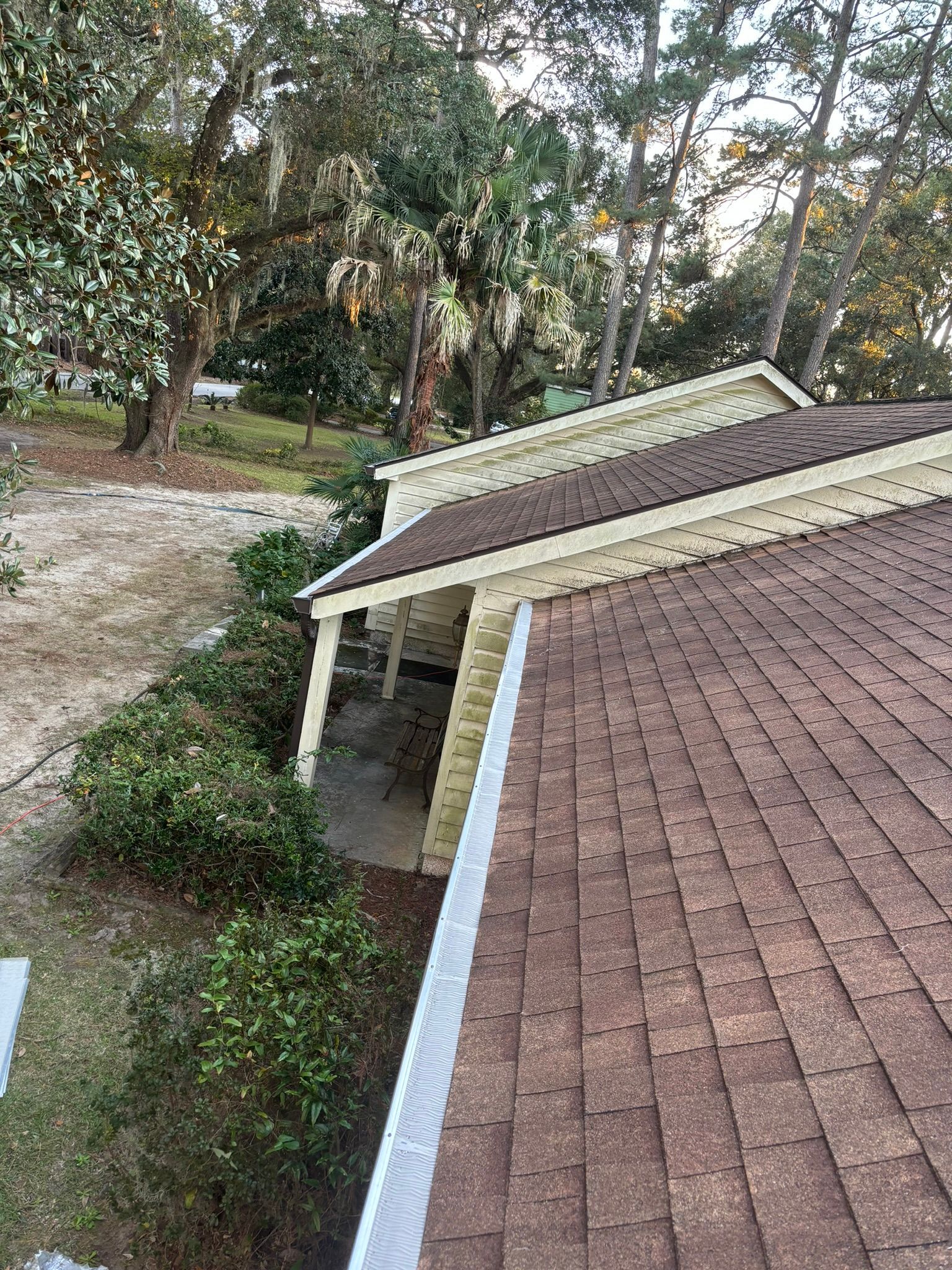 A high-angle view of a brown shingled roof with a white gutter running along the edge, overlooking a covered patio area.