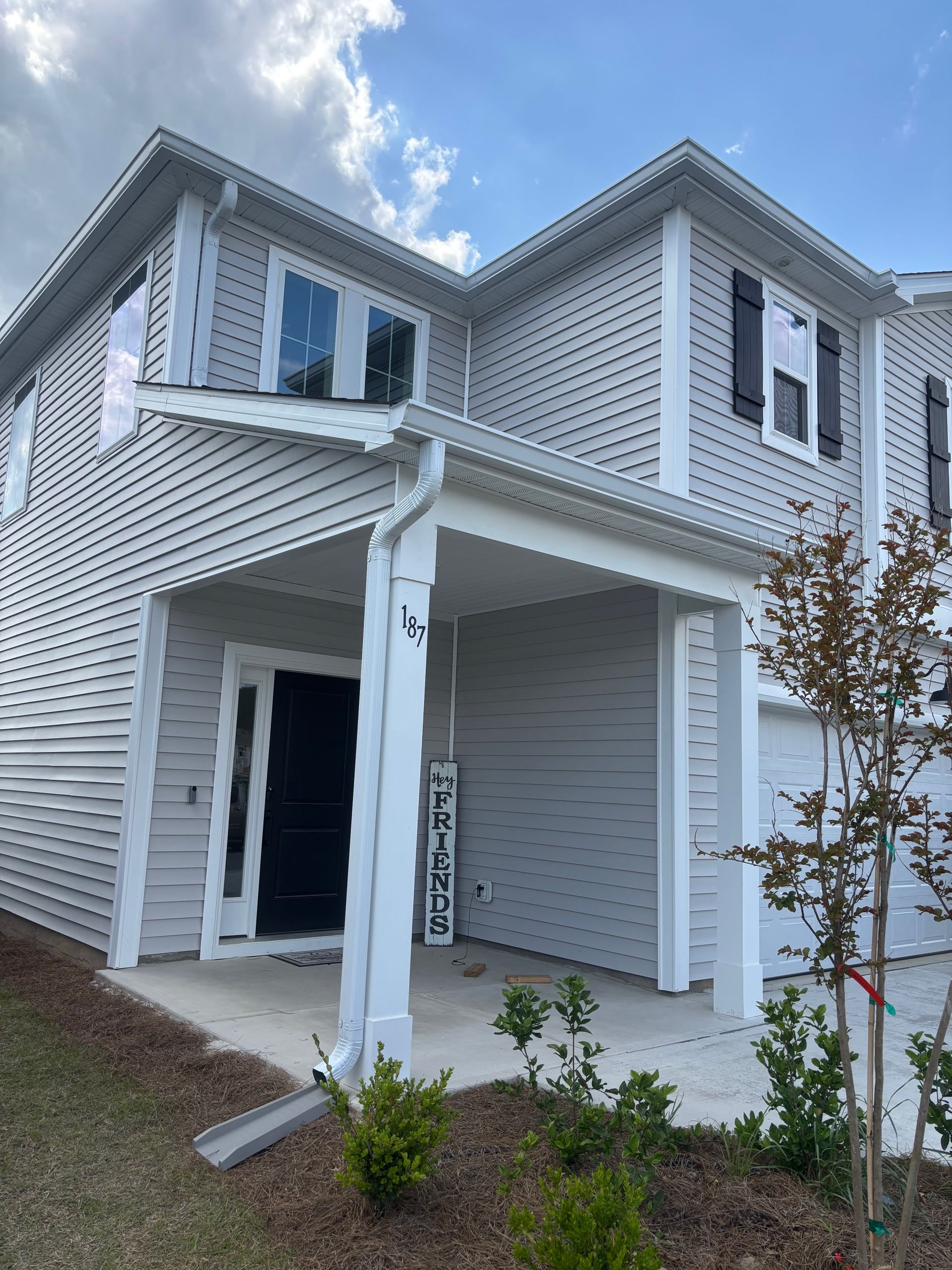 A two-story light gray house with a covered front porch, dark front door, and a white vertical welcome sign.