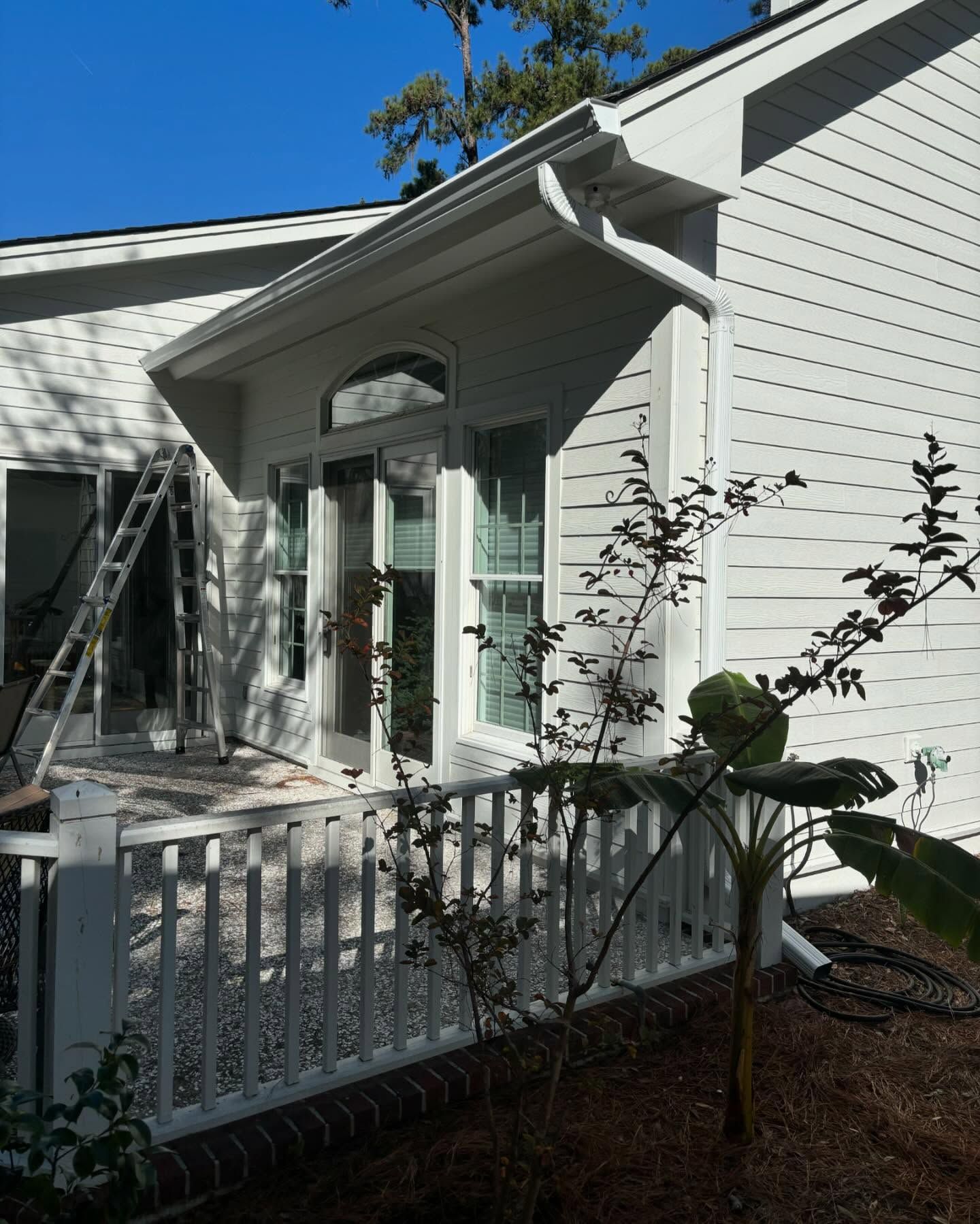 A white-sided home with a white porch railing, a glass-paned door, and a ladder leaning against the exterior wall.