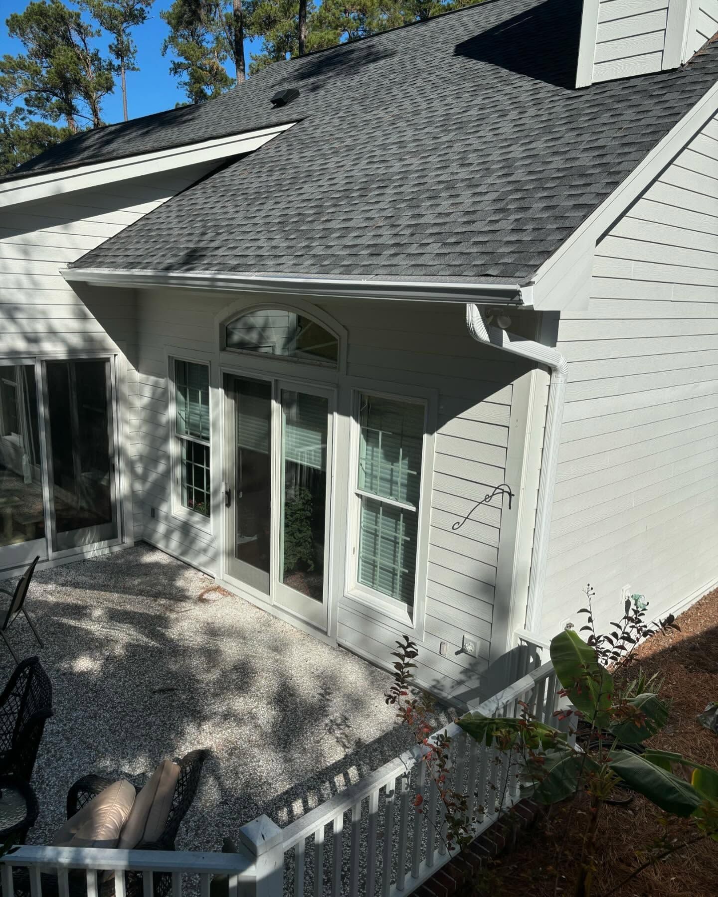 A high-angle view of a white, shingled-roof home exterior with French doors and a gravel patio area.