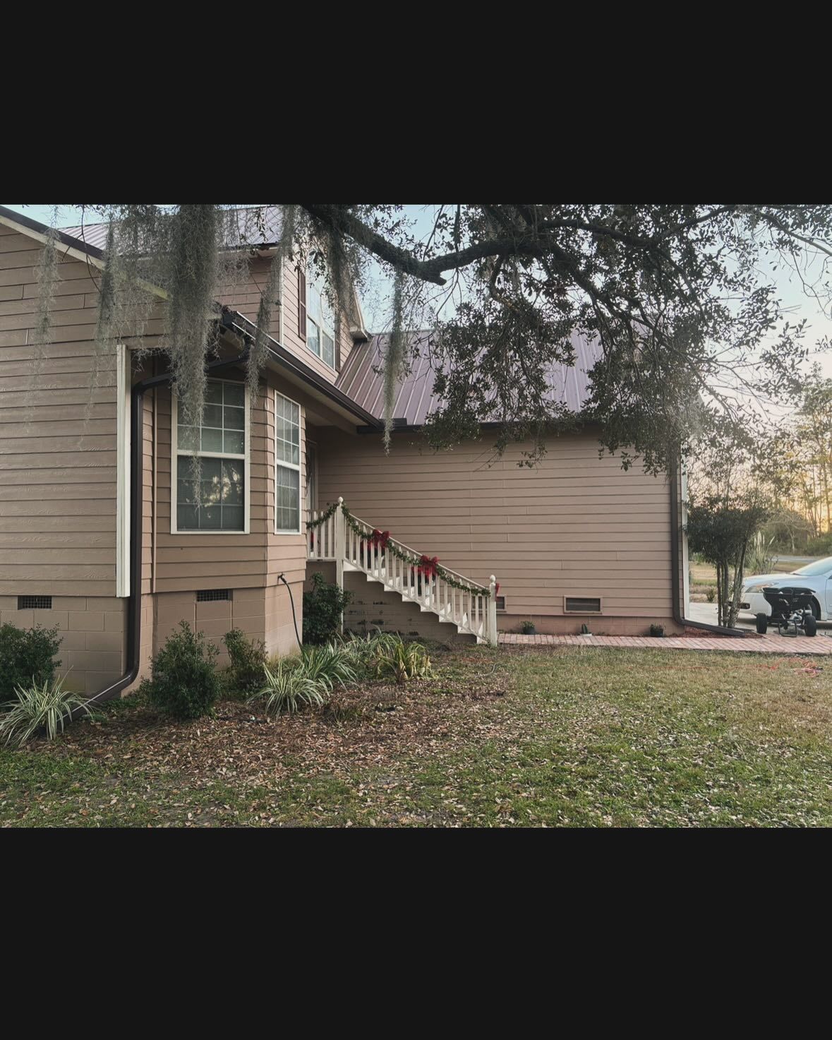 A tan, multi-story house with a metal roof and a staircase leading to a side door, framed by a large