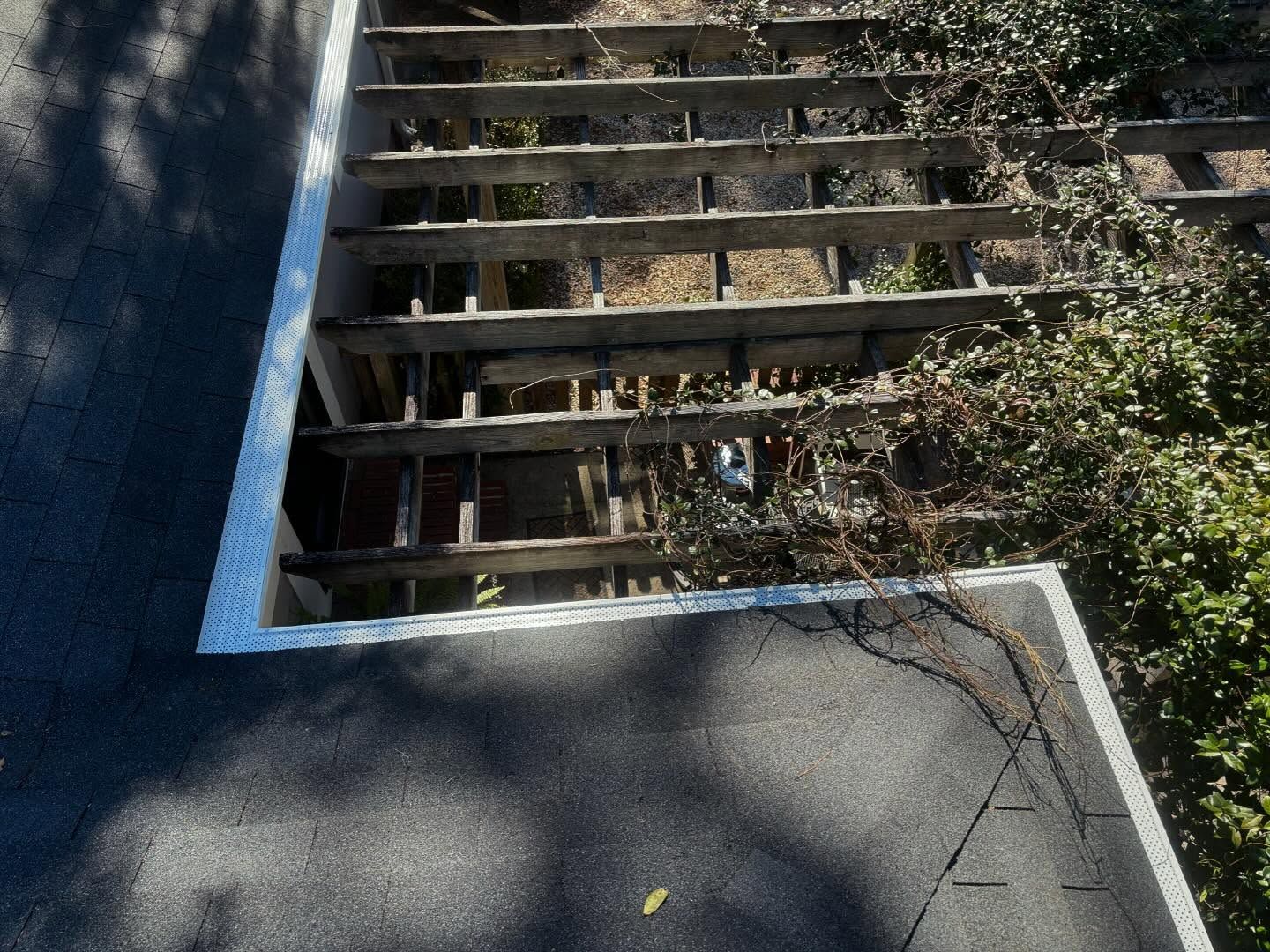 A roof section with a white-trimmed opening, revealing the wooden rafters of a pergola below.