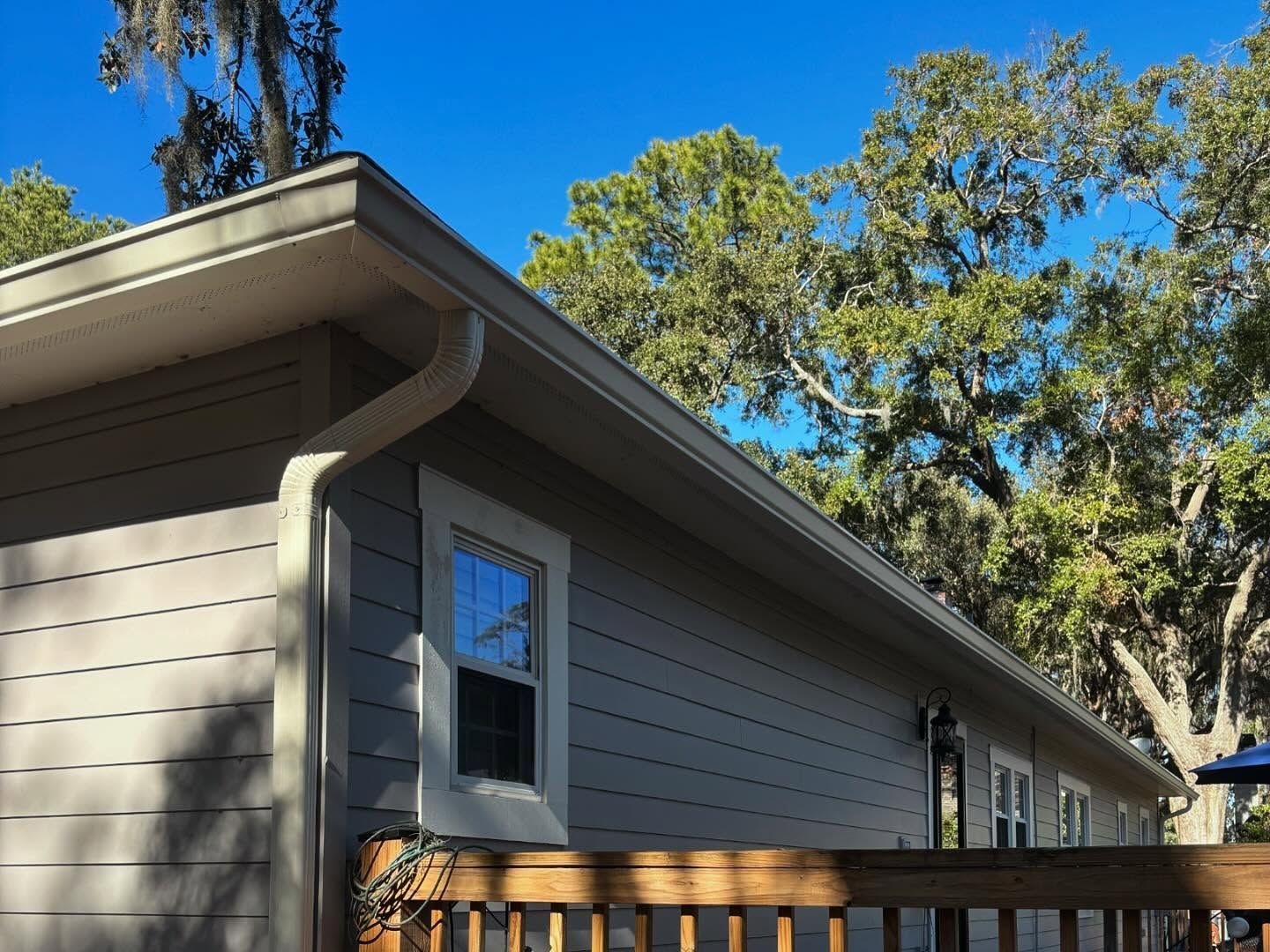 Exterior view of a gray-sided house with white trim, a gutter system, and a wooden deck railing against a blue sky.