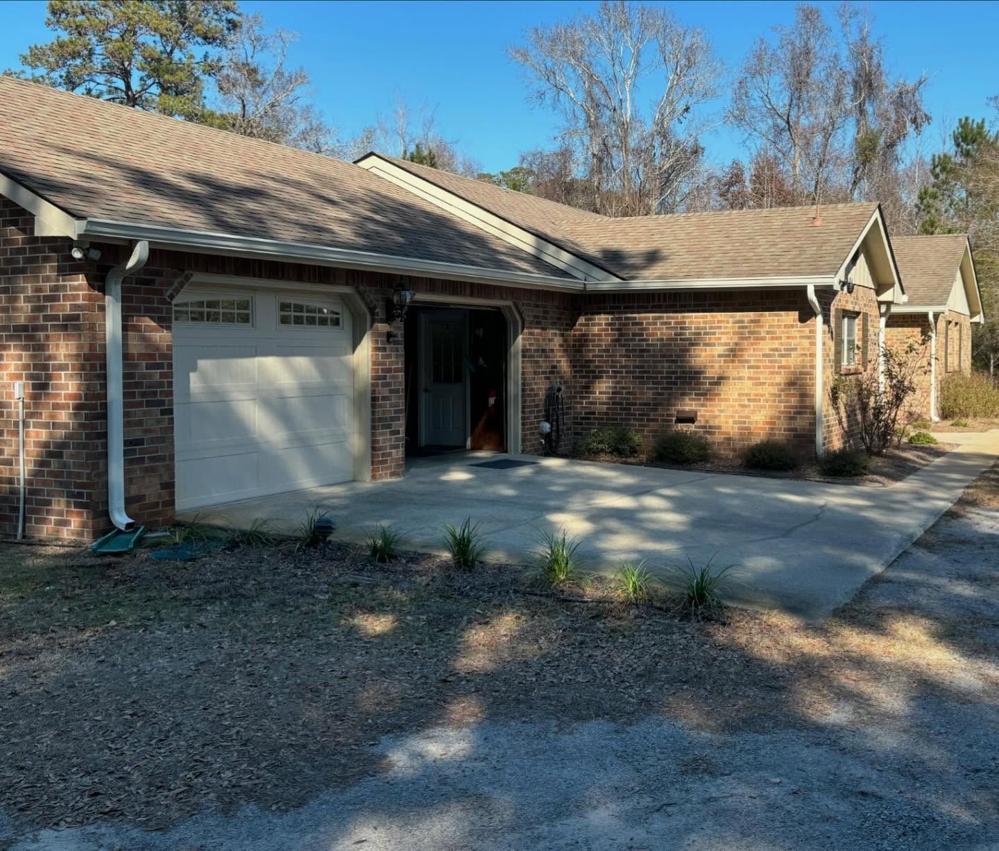 A single-story brick house with a concrete driveway and garage under a clear blue sky.