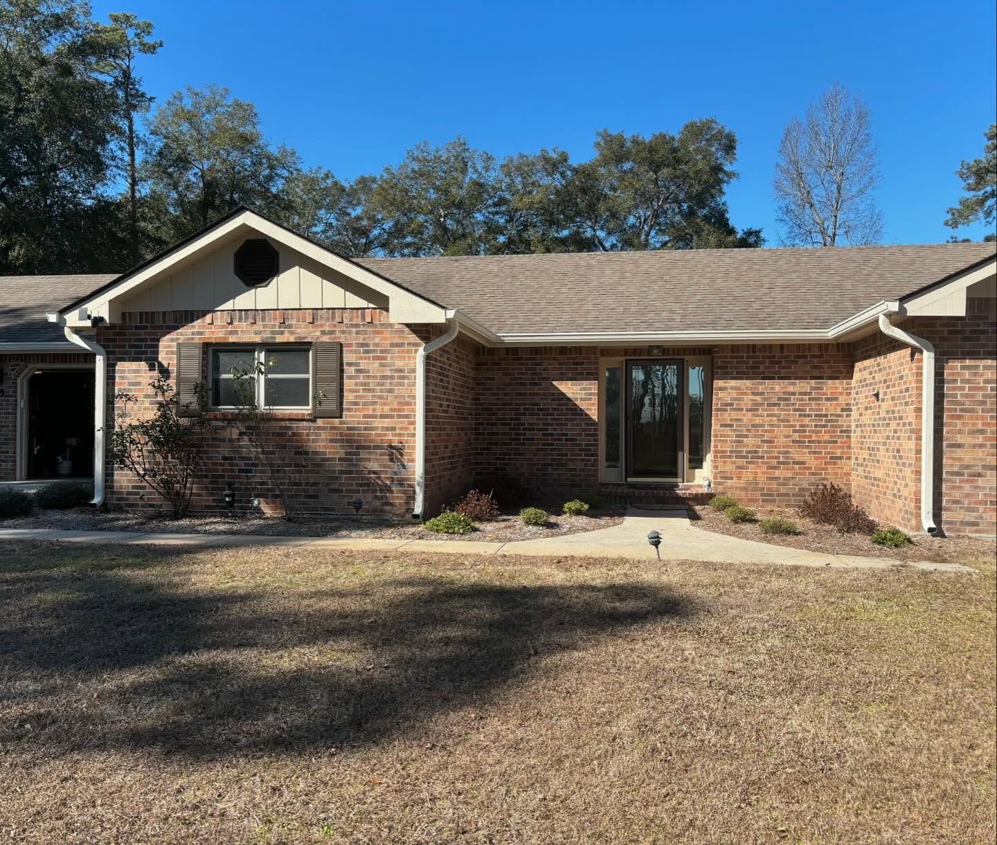 A single-story brick house with a brown shingled roof, a front entryway, and a circular vent in the front gable.