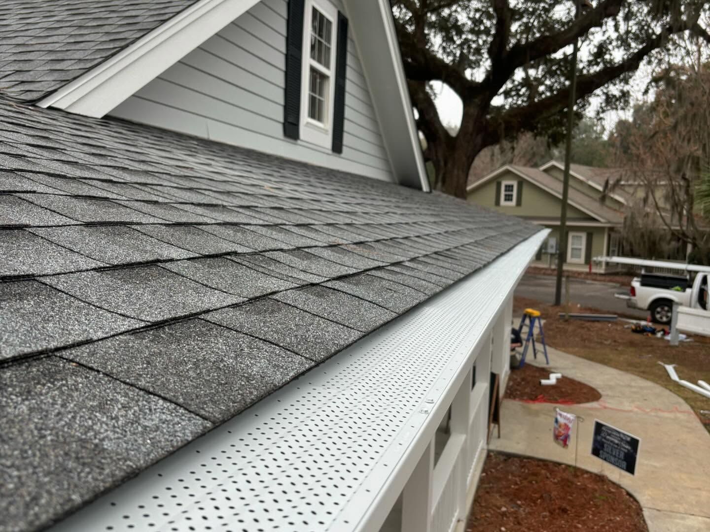 A close-up view of a shingled roof and a white, perforated gutter guard on a house exterior.
