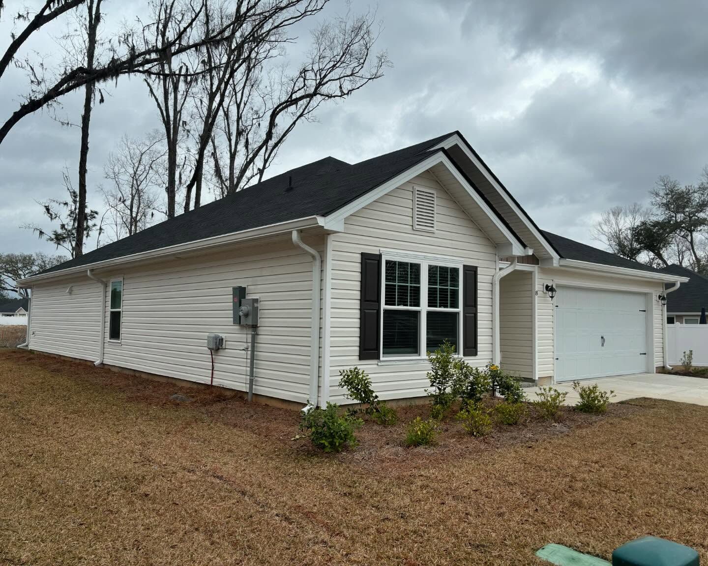 A single-story, light-colored suburban house with a two-car garage, dark shutters, and a dark shingled roof.