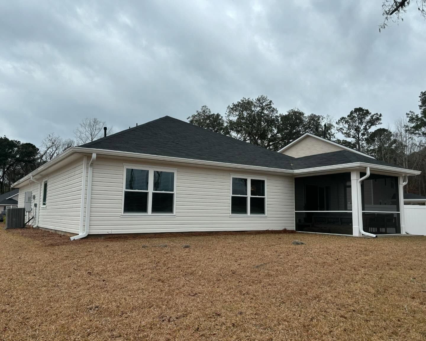 A single-story, light-colored vinyl-sided house with a dark shingle roof and a screened-in back porch.