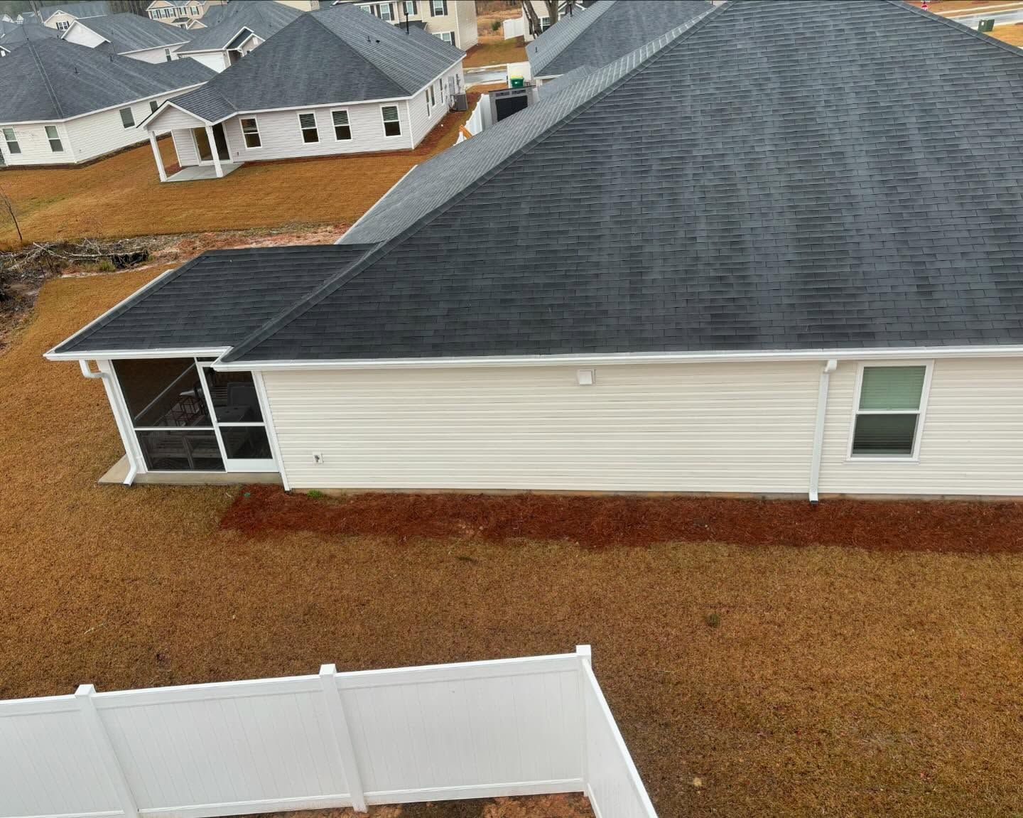 An aerial view of a single-story house with a white exterior, gray shingled roof, and a screened-in porch.