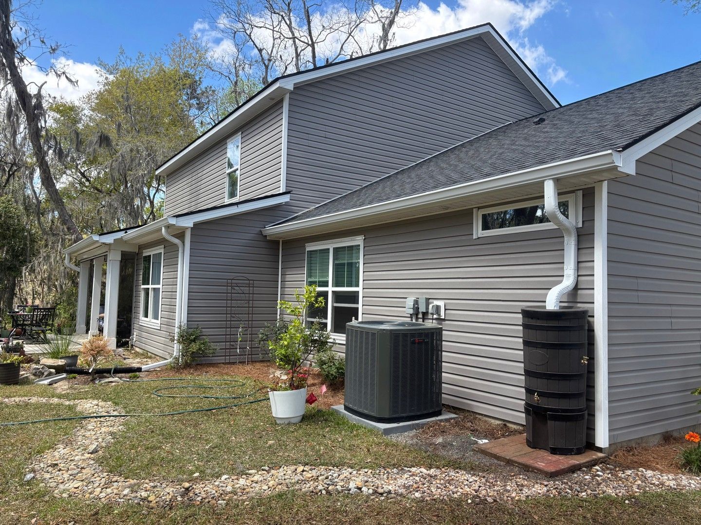 A gray two-story house with siding, a side-yard air conditioning unit, and a rain barrel attached to the gutter.