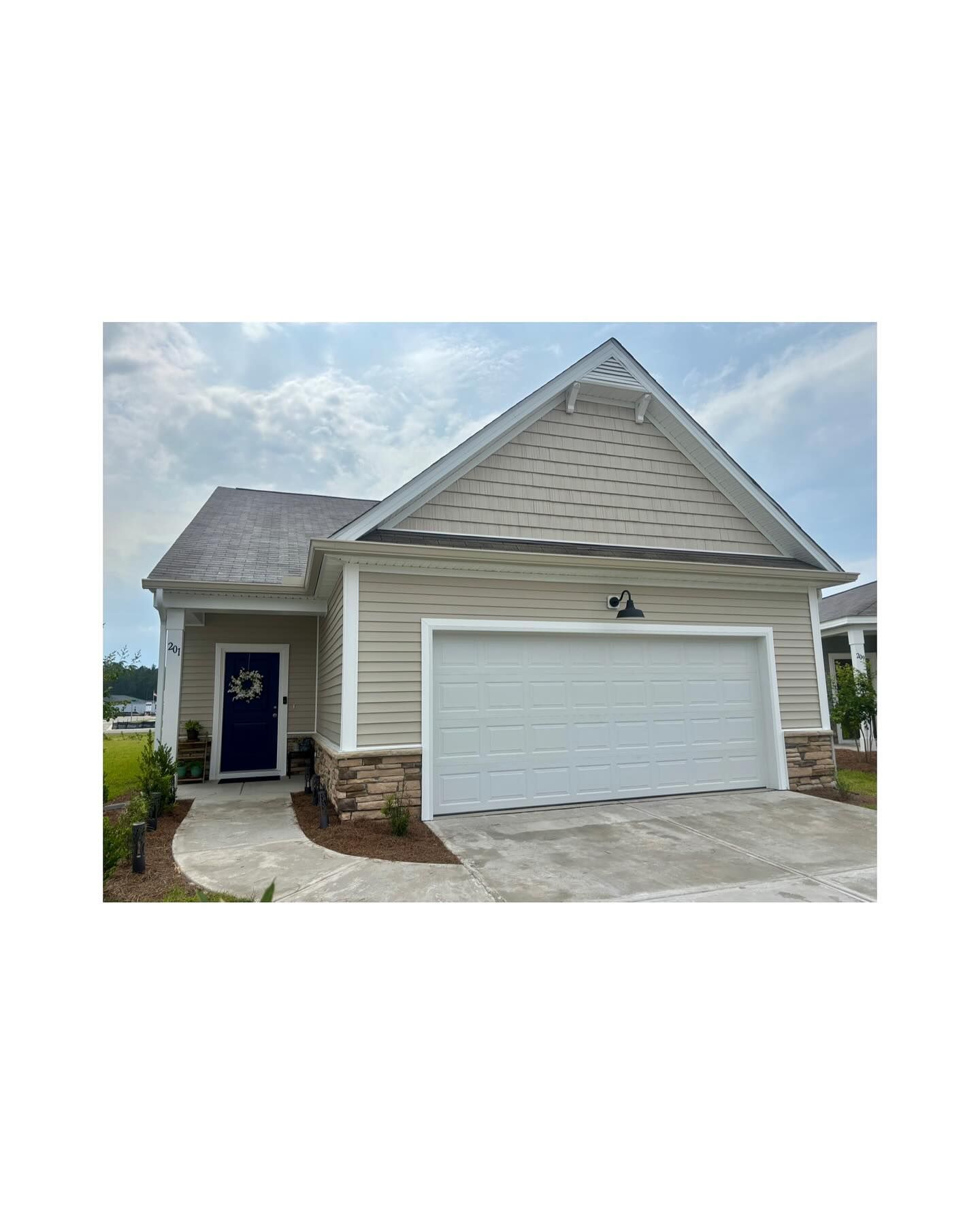 A single-story suburban house with beige siding, a two-car garage, stone veneer base, and a dark blue front door.