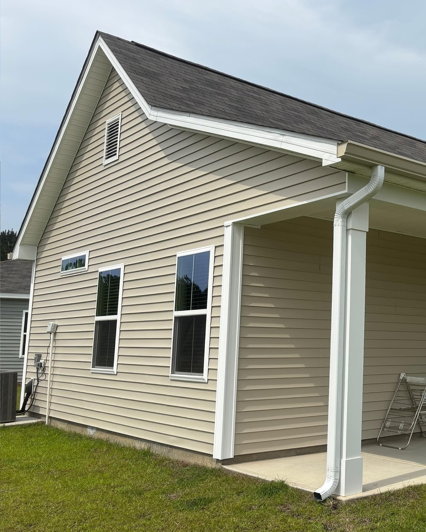 Beige siding on the exterior of a house with a covered porch, white trim, and a gabled roof against a bright sky.