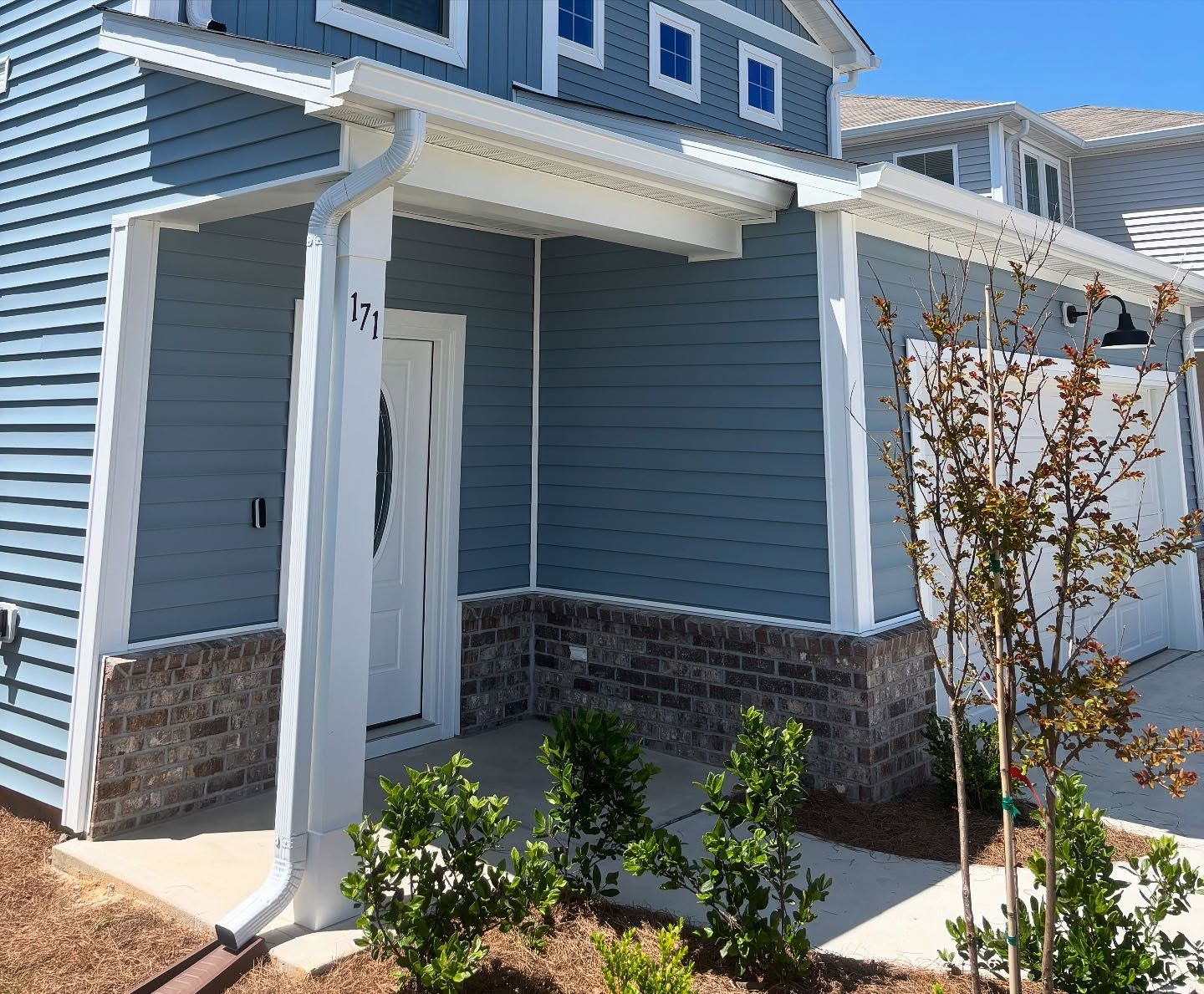 Blue house exterior with stone accents, white door, and a small porch area in front of a concrete driveway.