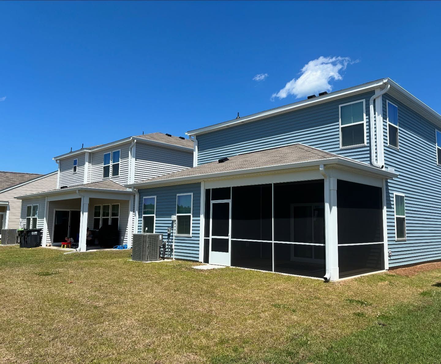 Two blue houses with light-colored trim and screened-in back porches under a clear blue sky.