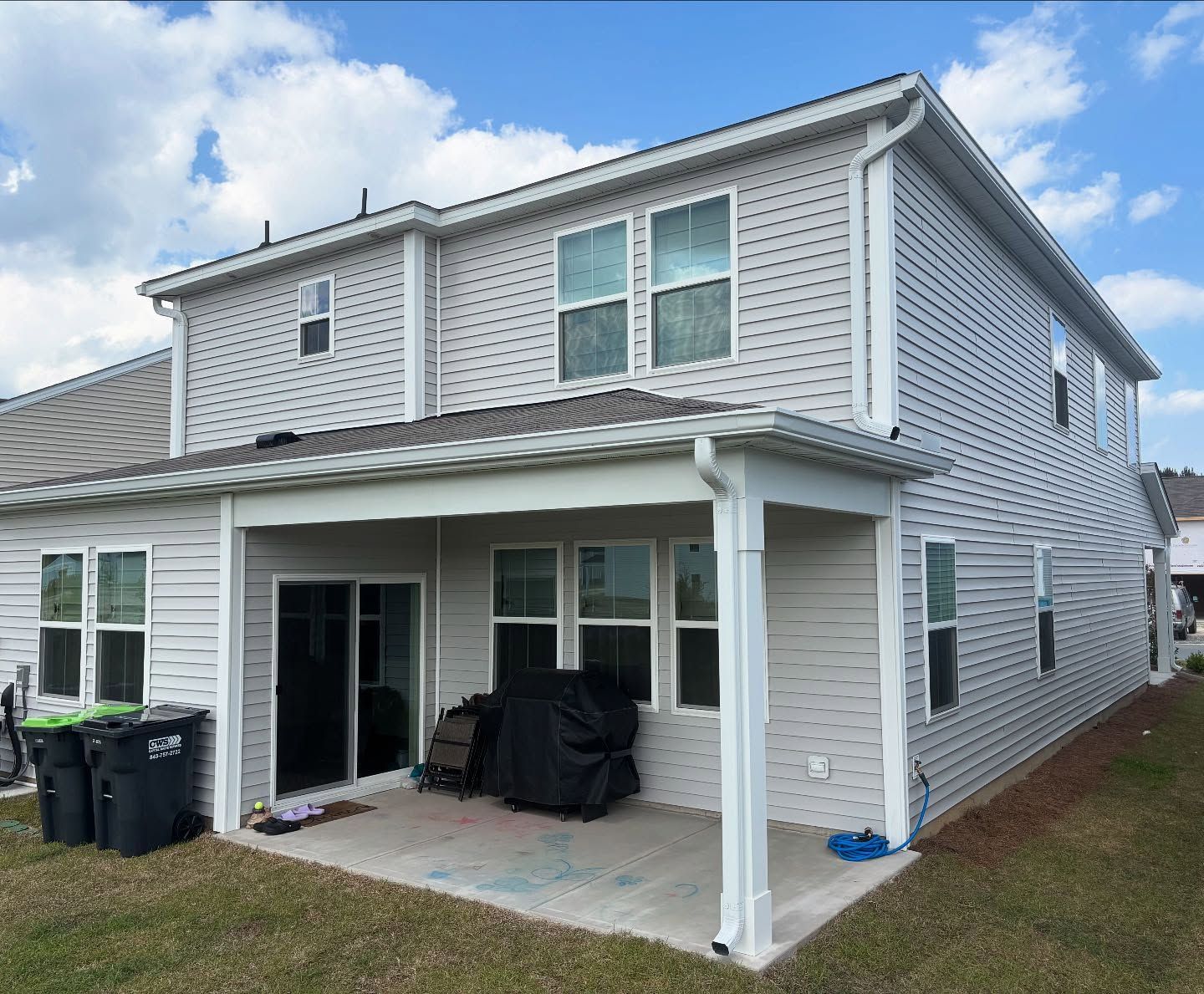 A two-story light gray vinyl-sided house with a covered concrete back patio, sliding glass door, and yard.