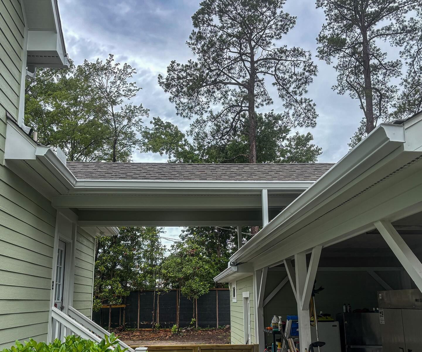 A light-green house with a covered walkway connecting a doorway to a garage under a cloudy sky.