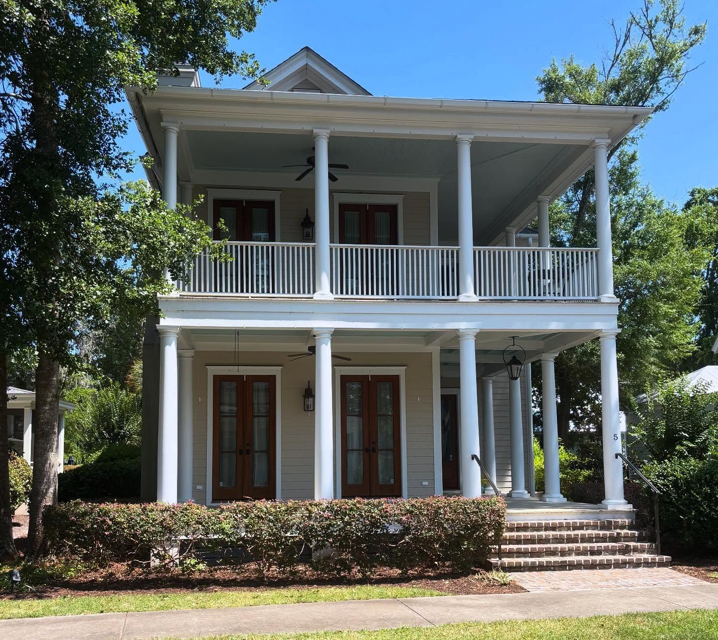 A two-story, beige Southern-style home with white columns, a full-length front porch, and a white balcony railing.