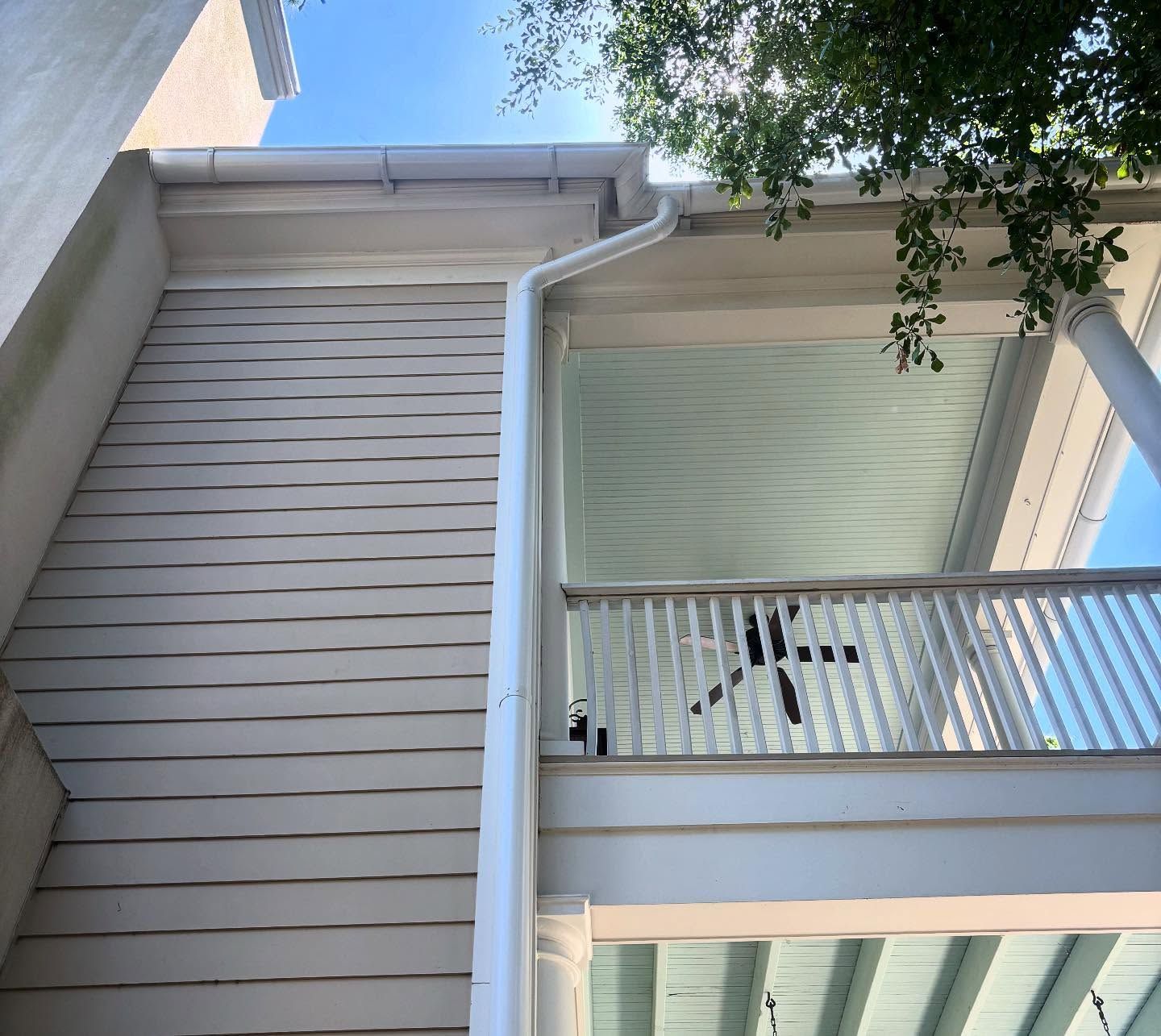 A two-story porch with beige horizontal siding, a white gutter downspout, white railings, and a light blue beadboard ceiling.