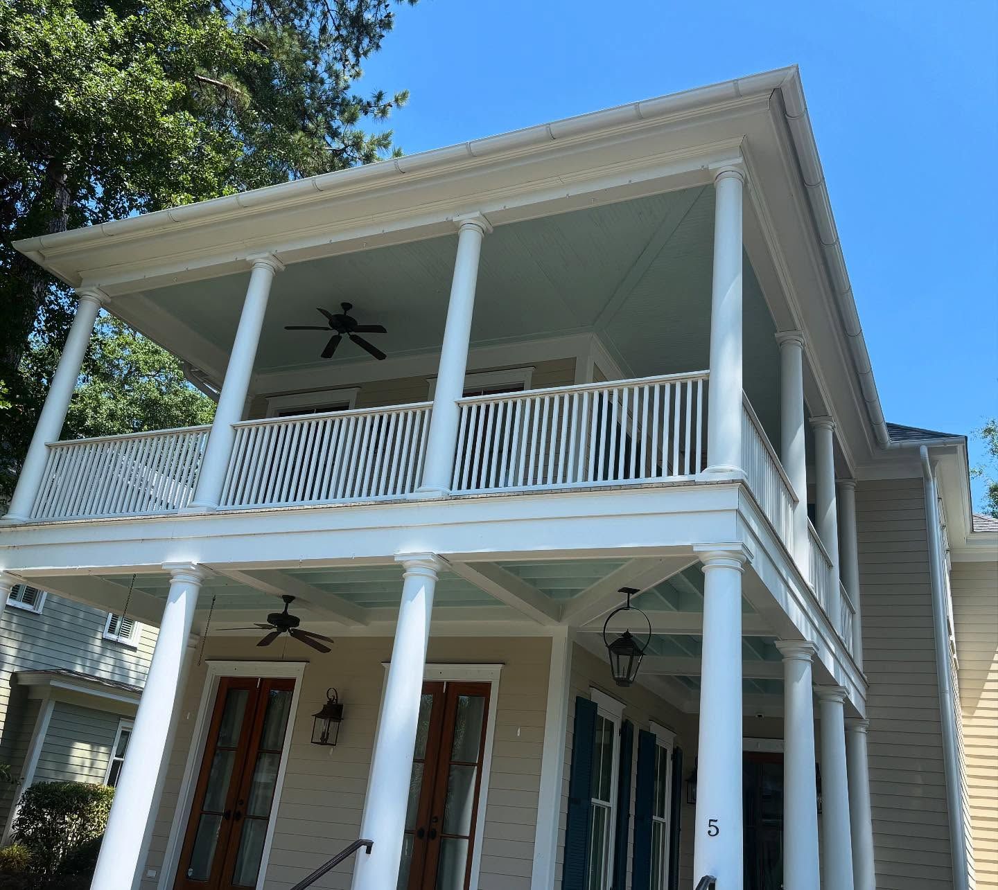 A beige two-story house with a double-decker white porch, tall columns, ceiling fans, and blue porch ceilings.