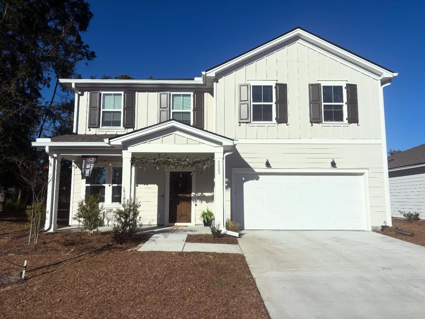 A two-story, light-colored suburban house with a covered front porch, a two-car garage, and dark window shutters.