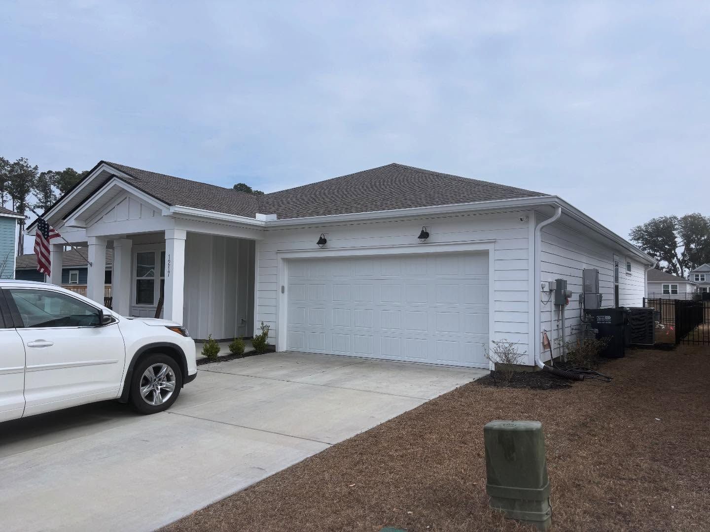A white, single-story suburban house with a two-car garage and a front porch, featuring a white car parked in the driveway.