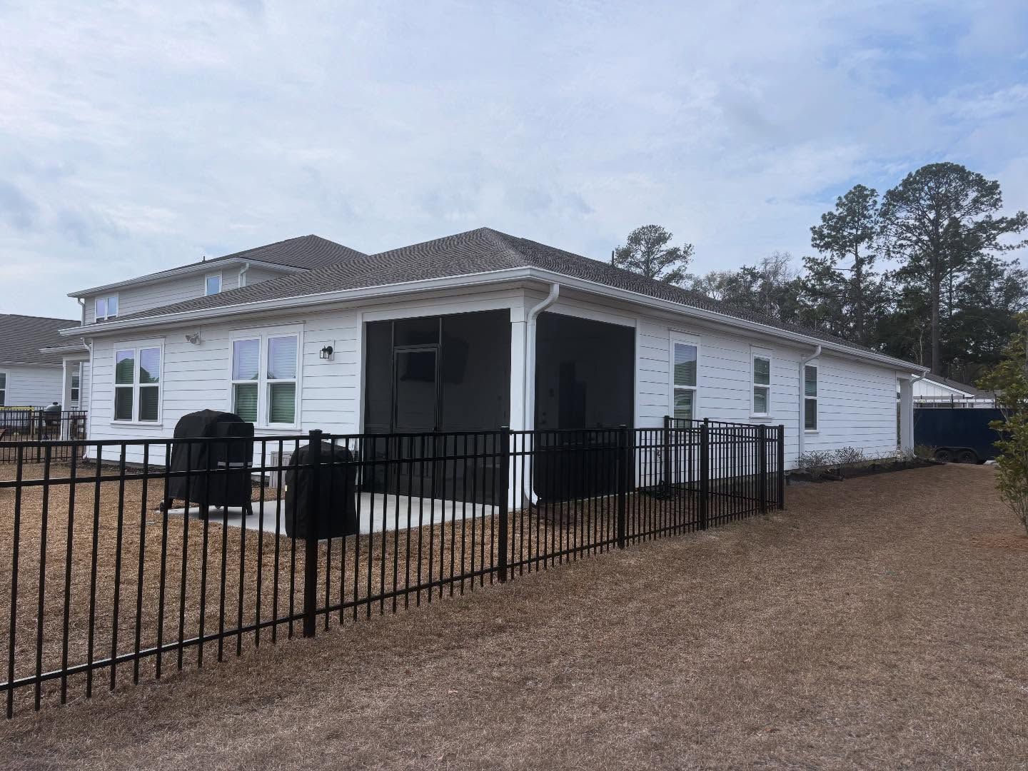 A white house with a screened-in porch and a black metal fence in a yard with mulch ground cover.