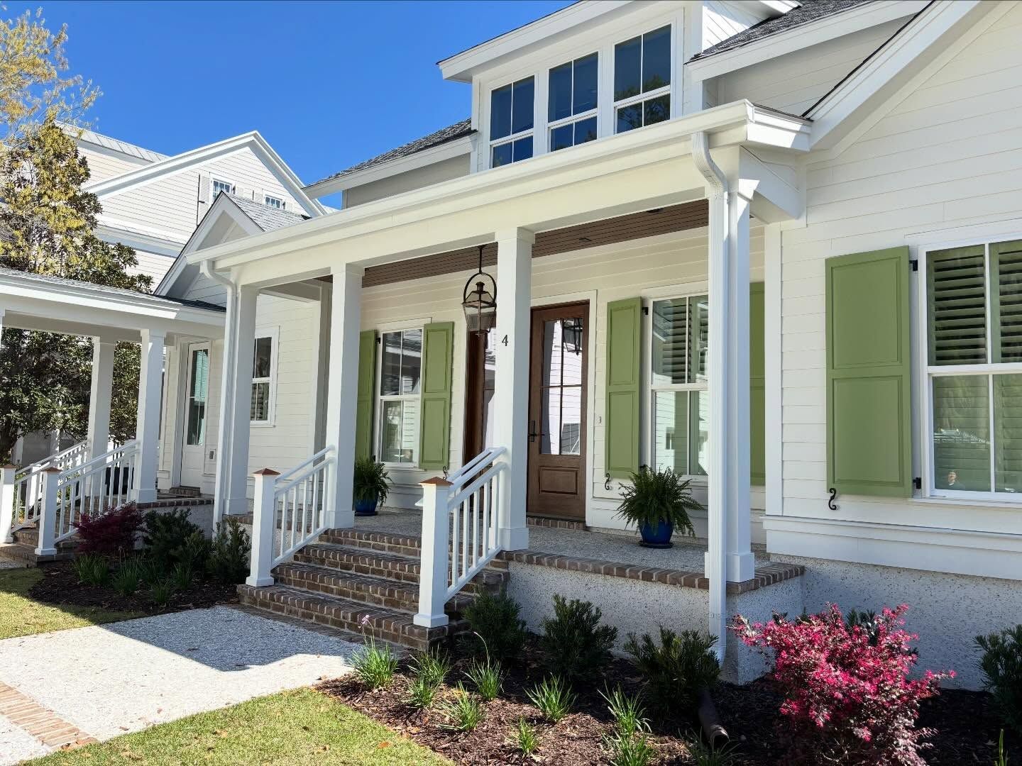 White suburban house with a front porch, light green shutters, and a brick-stepped entrance on a sunny day.