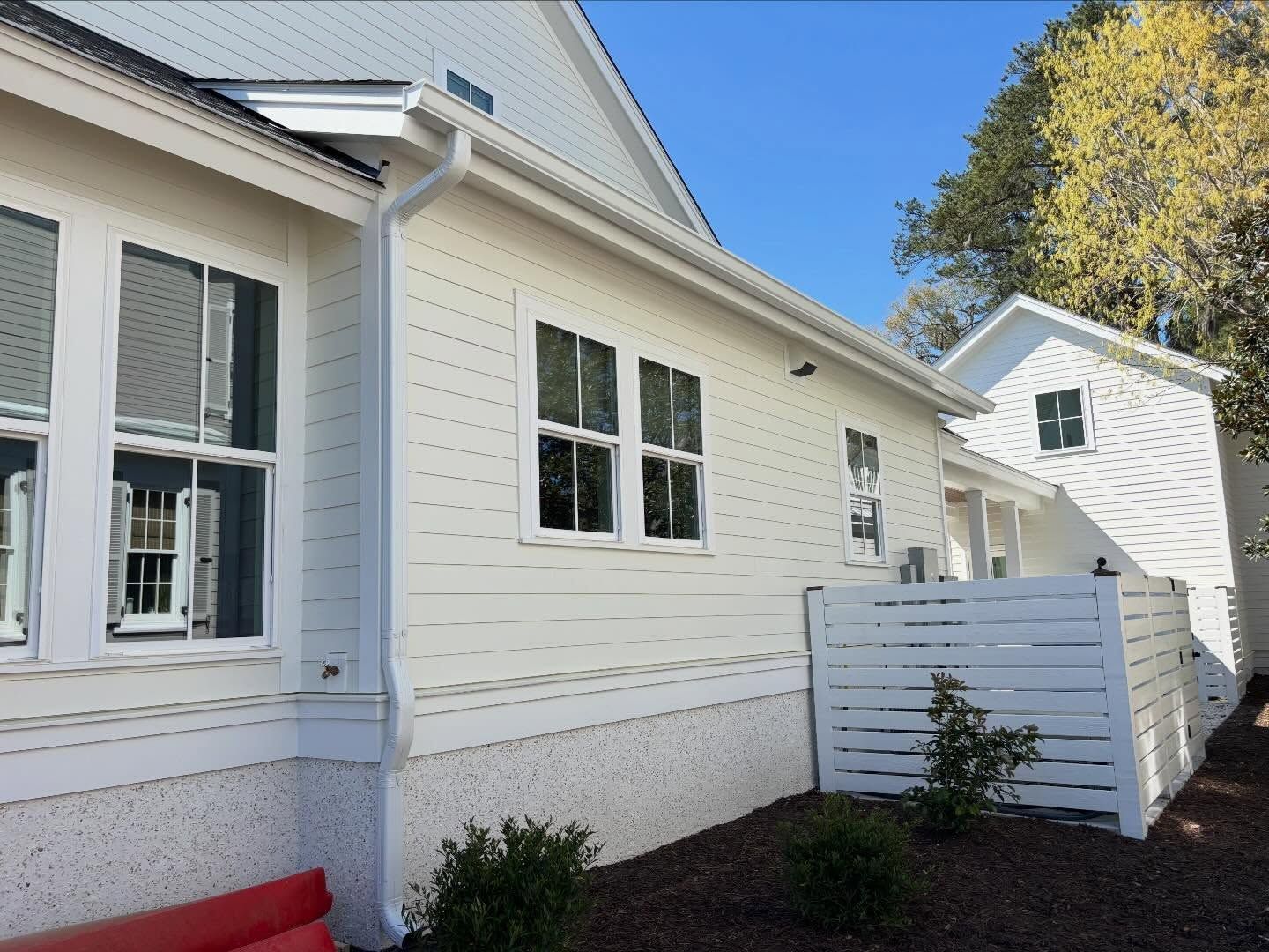 White siding house with a prominent white downspout and a small white wooden privacy fence in a landscaped yard.