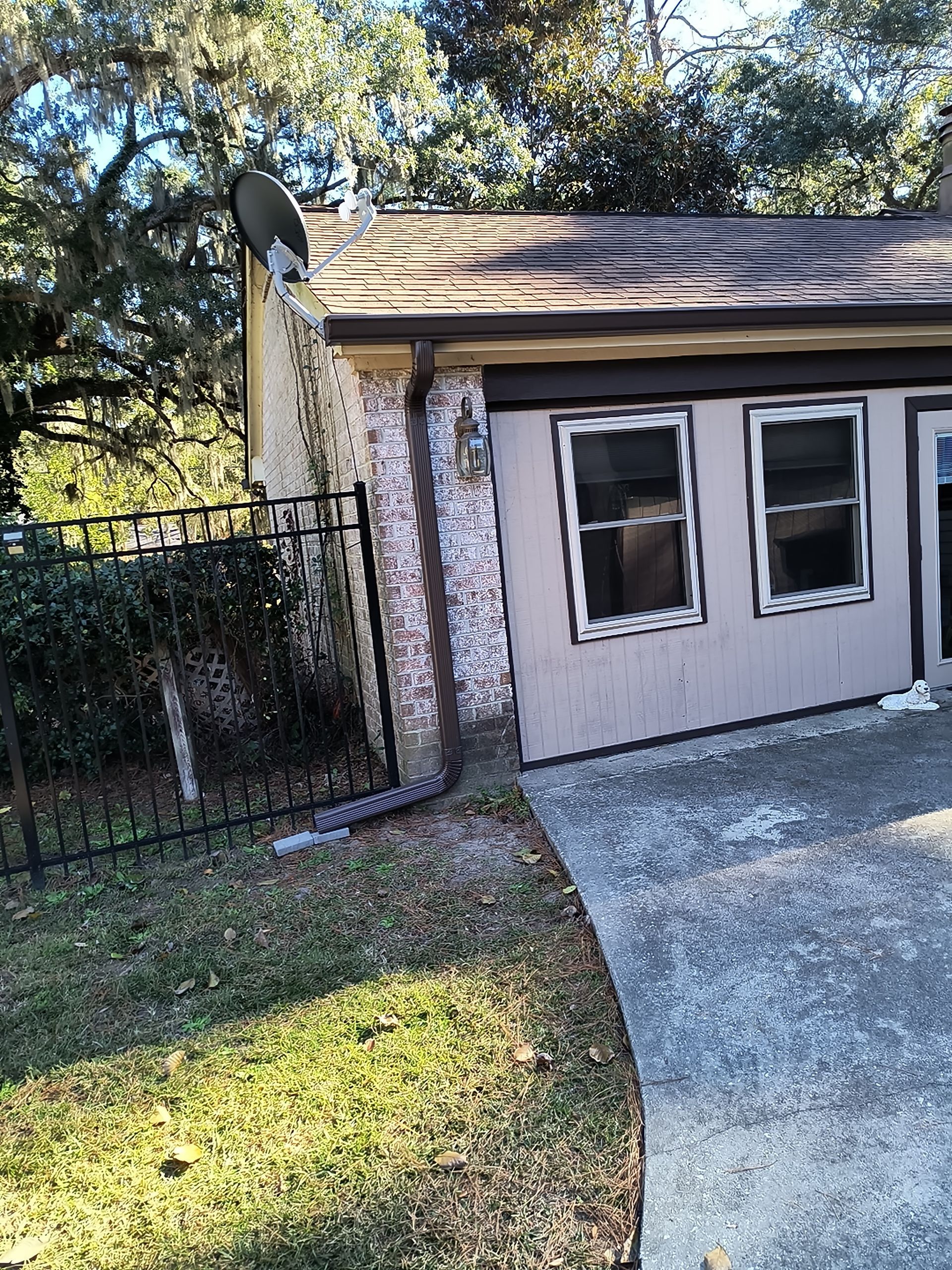 A low-angle view of a detached garage with textured white siding, two windows, and a satellite dish on its roof.