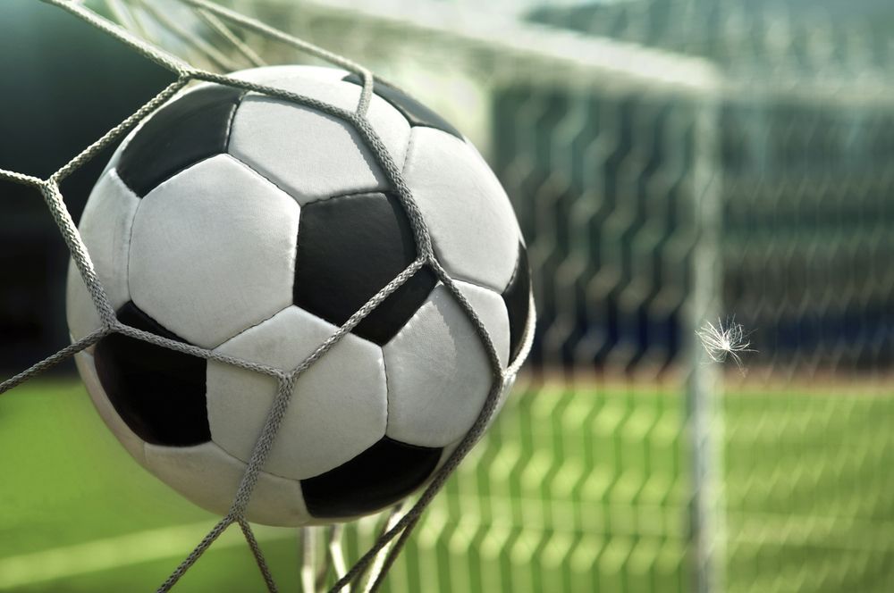 Soccer ball in net, black and white ball, green field background.