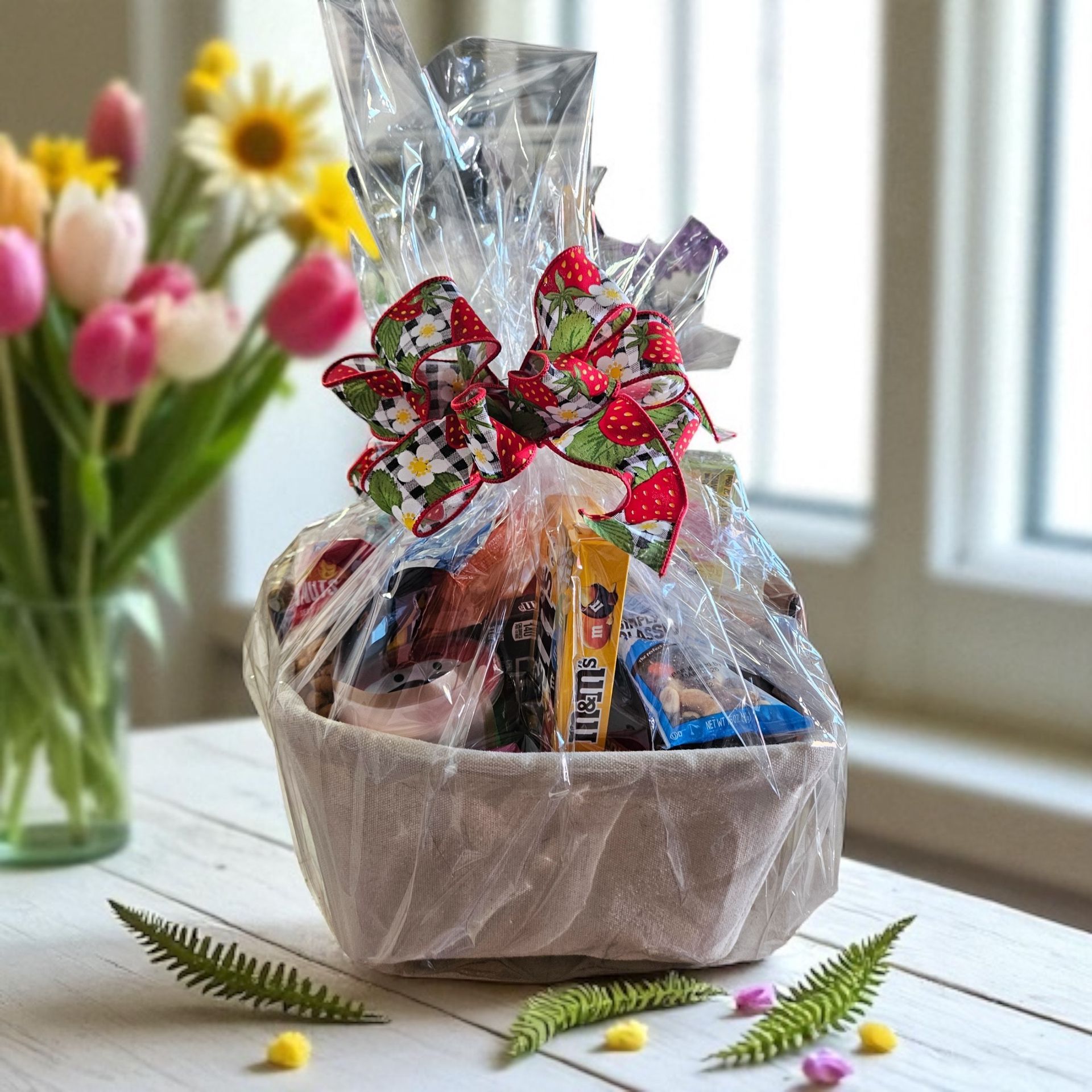 Easter gift basket with red floral bow, cellophane wrap, and tulips on a table.
