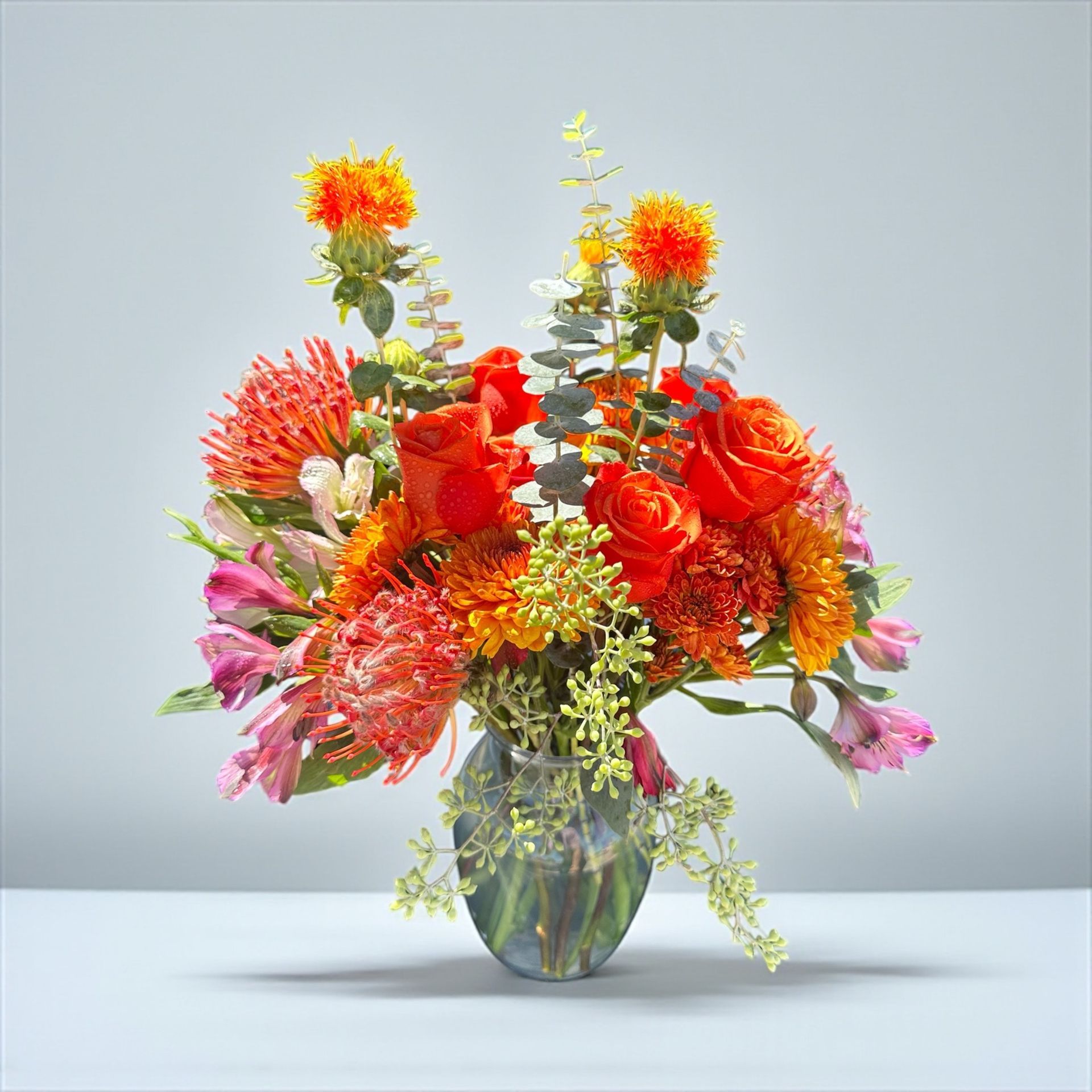 Vibrant orange and pink flower bouquet in a clear glass vase.