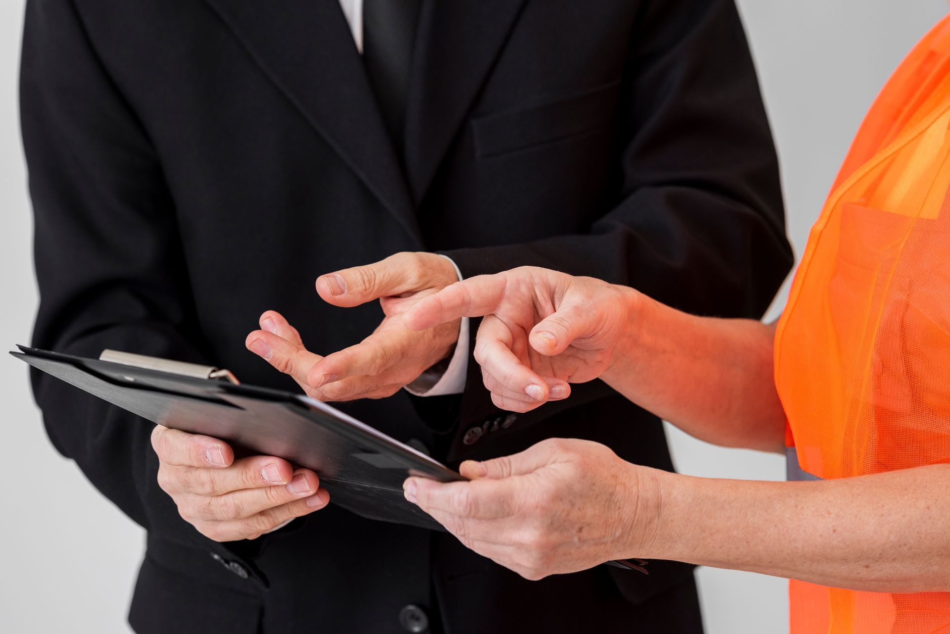 A man in a suit and a woman in an orange vest are looking at a clipboard.