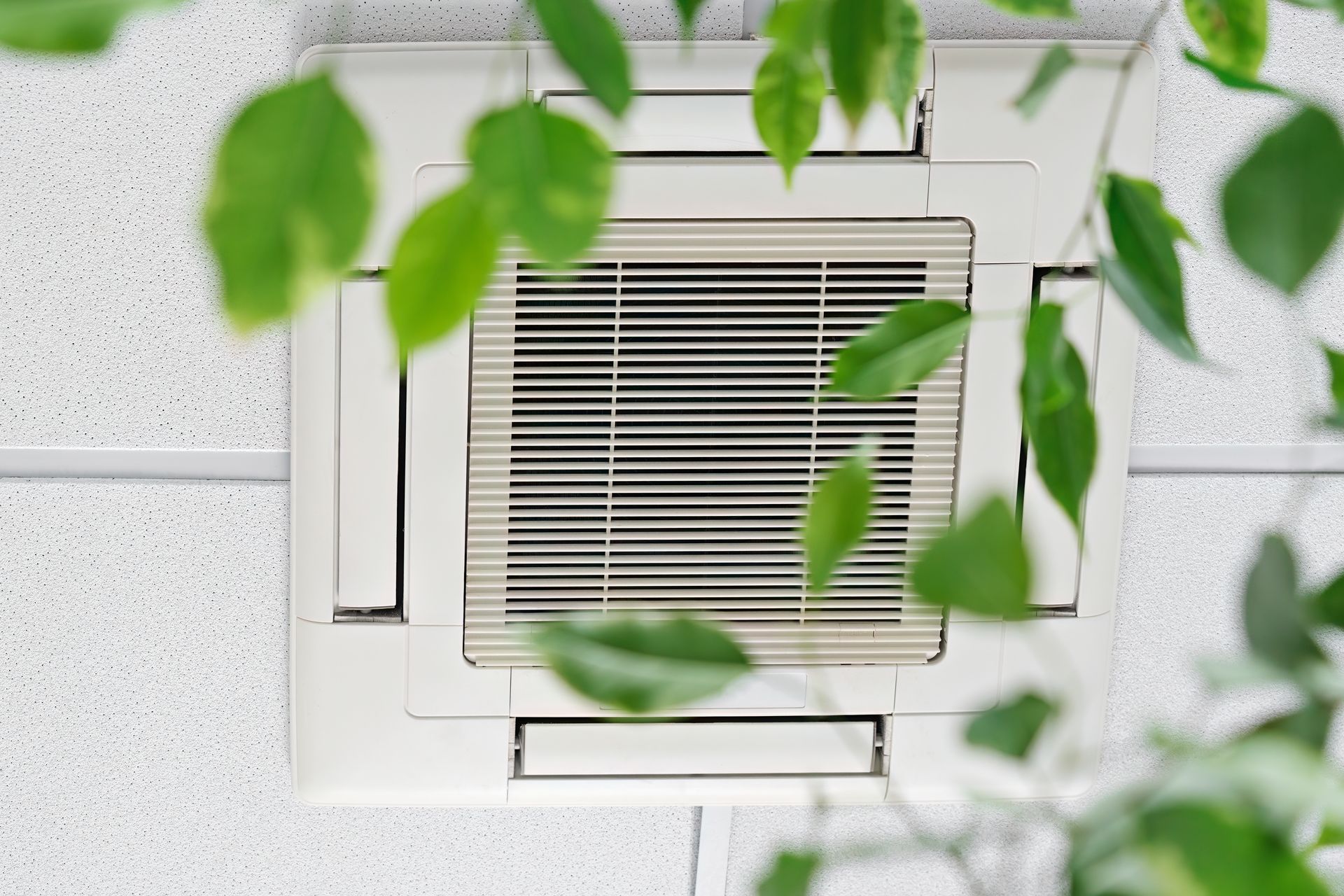 A close up of a ceiling fan with green leaves surrounding it.