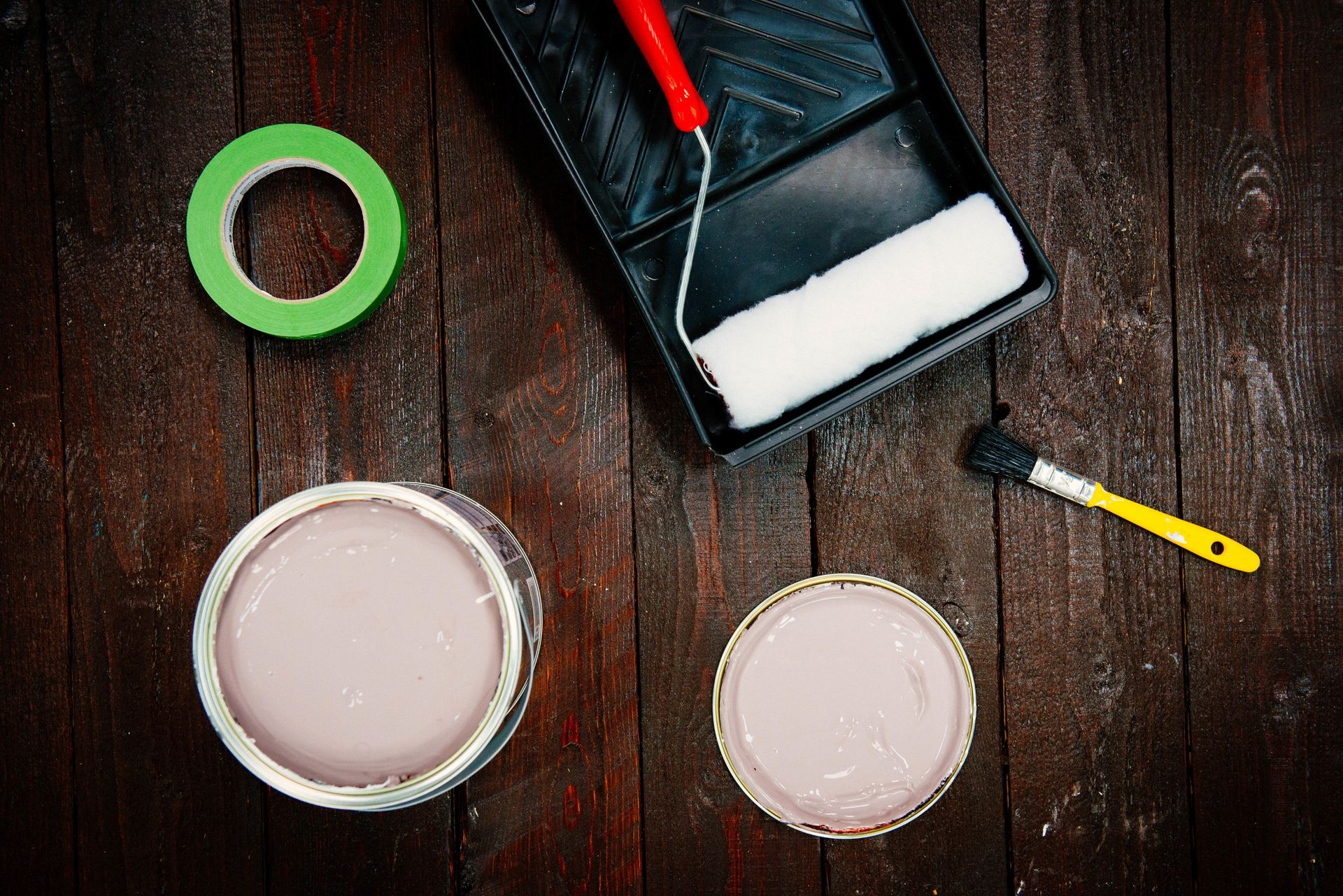 A tray of paint , a paint roller , a brush , and tape on a wooden table.