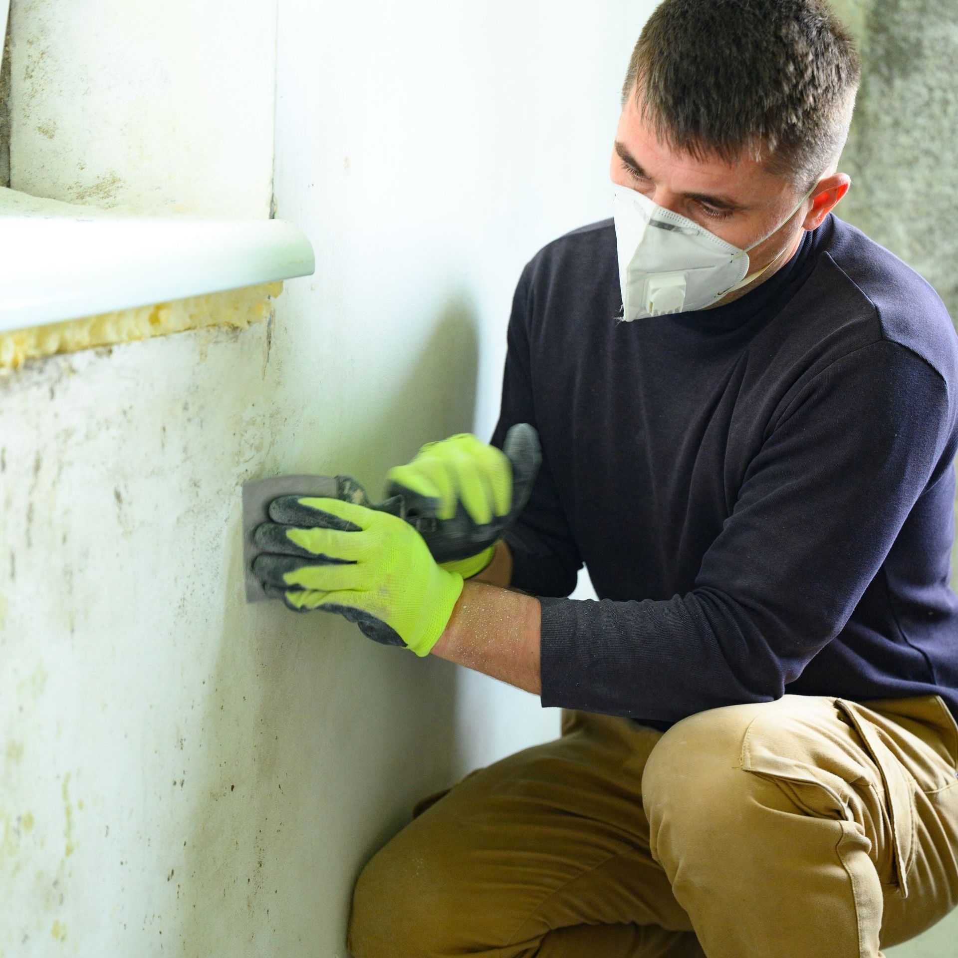A man wearing a mask and gloves is cleaning a wall.
