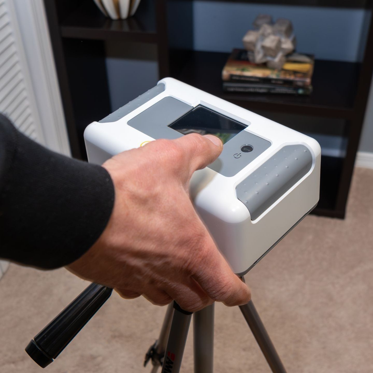 A person is holding a white radon testing device on a tripod