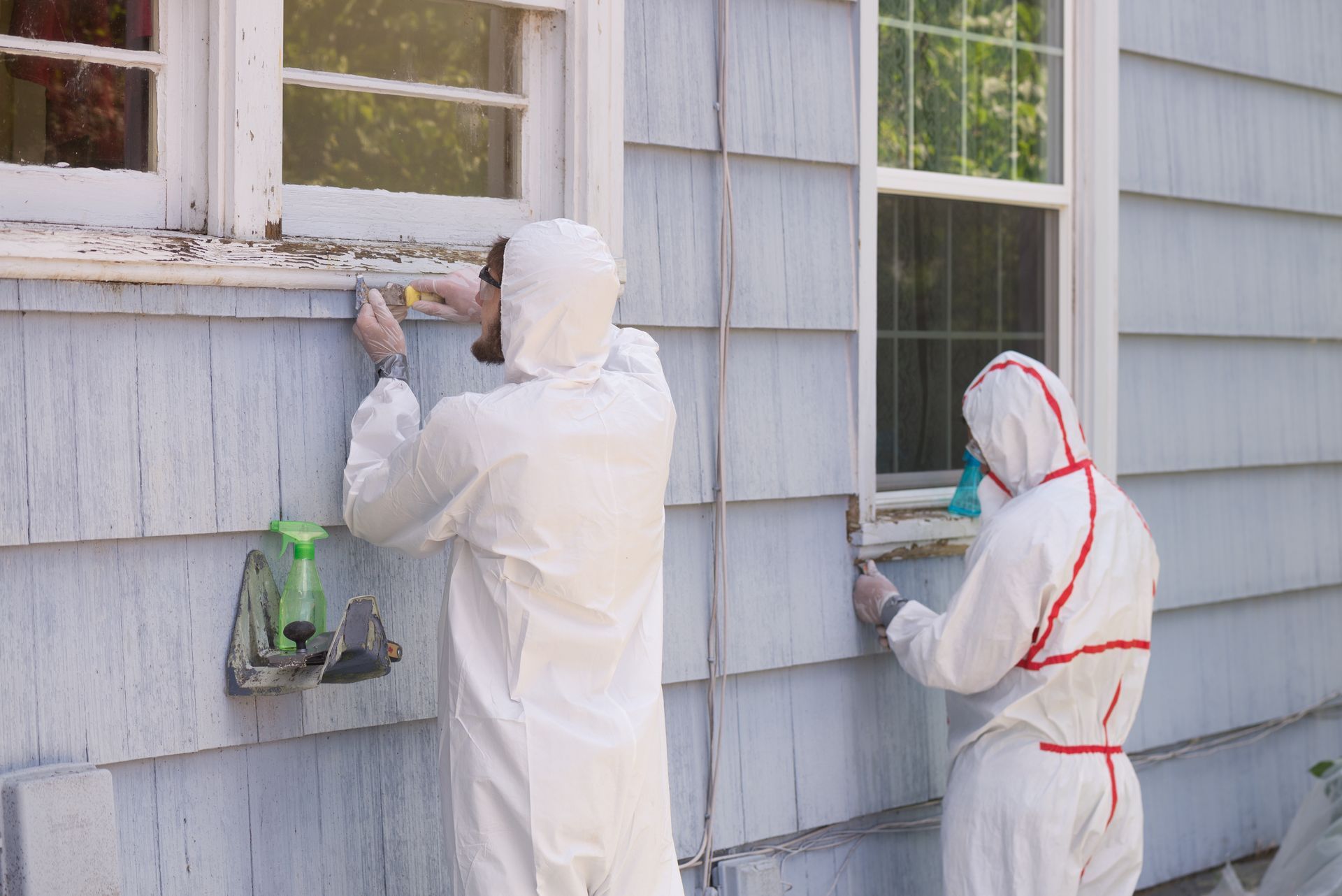 Two men in protective suits are working on the side of a house.