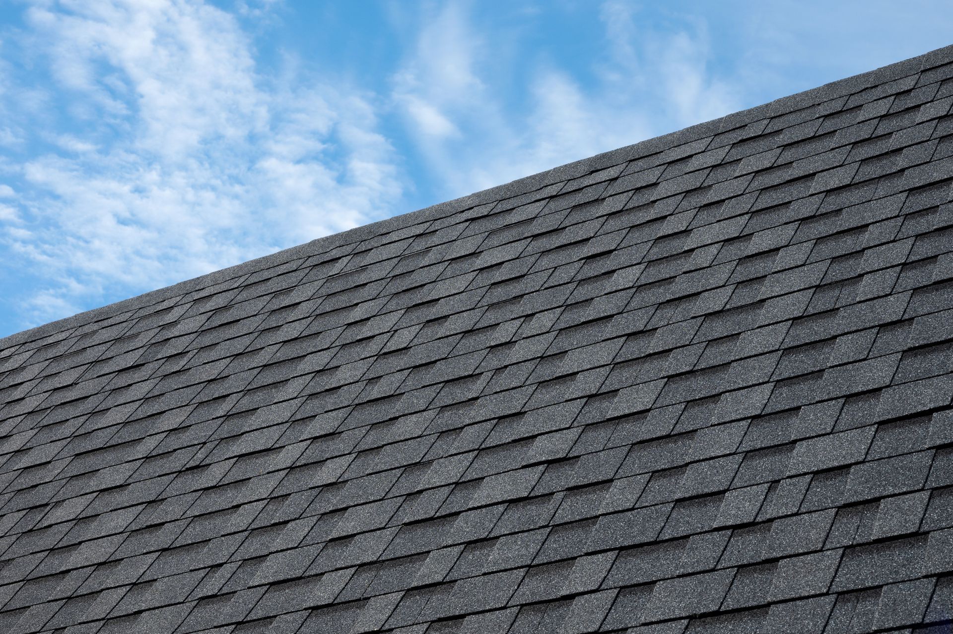 Tab-style asphalt roof shingles installed on a commercial building under a clear blue sky.