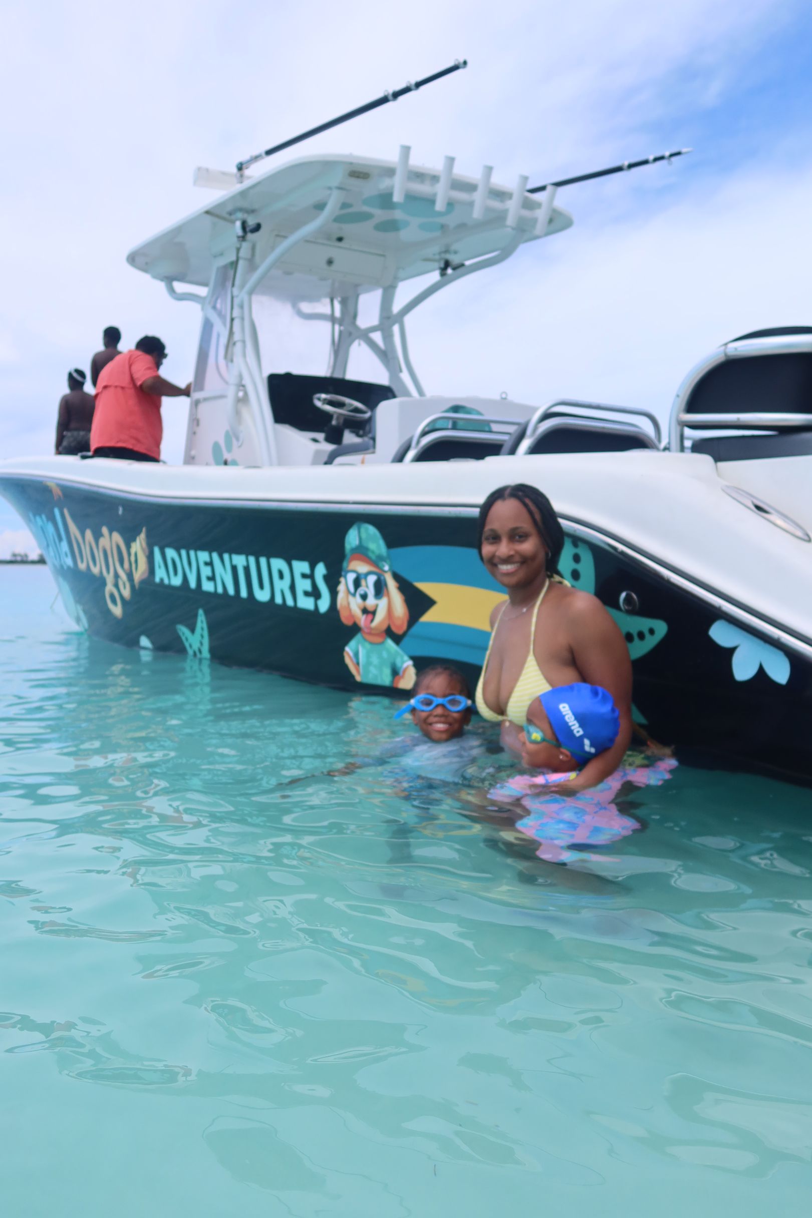 Woman smiling in turquoise water beside a white boat with “ADVENTURES” on the side