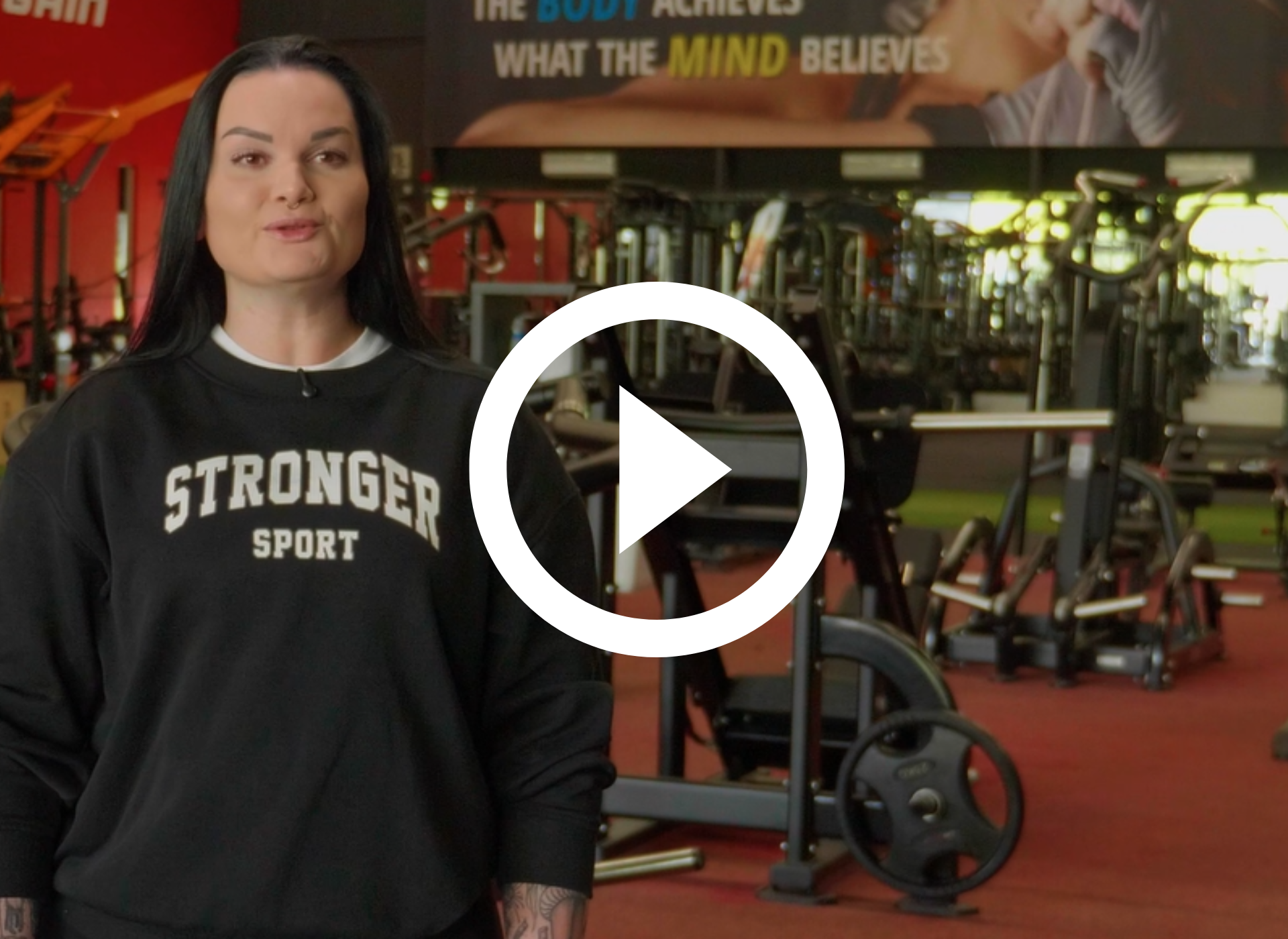 Een vrouw in de sportschool praat tegen de camera. Op de achtergrond zijn andere mensen aan het sporten.