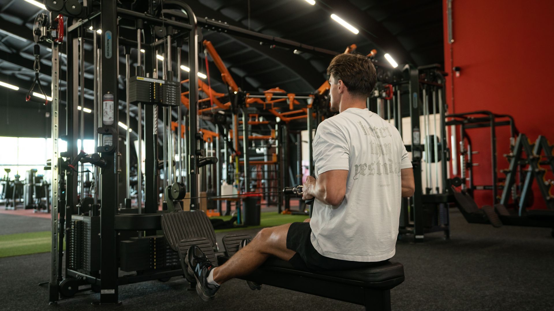 Een man zit op een roeimachine in een sportschool. Hij trekt de kabel naar zijn borst.
