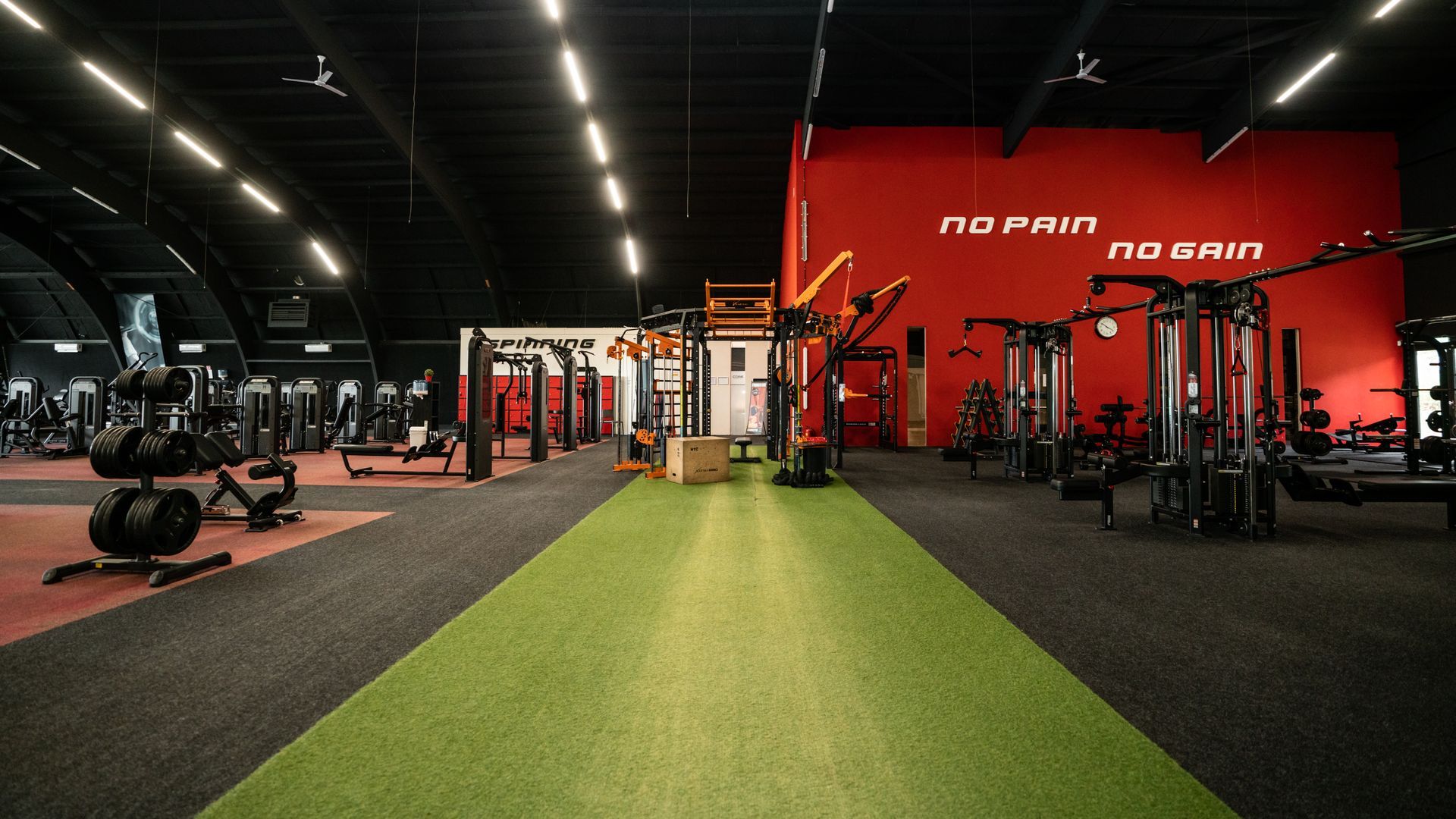 Interieur van een sportschool met fitnessapparatuur op een groene en zwarte vloer, rode muren en de tekst