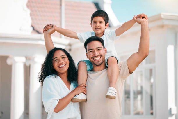 A man is carrying a child on his shoulders in front of a house.