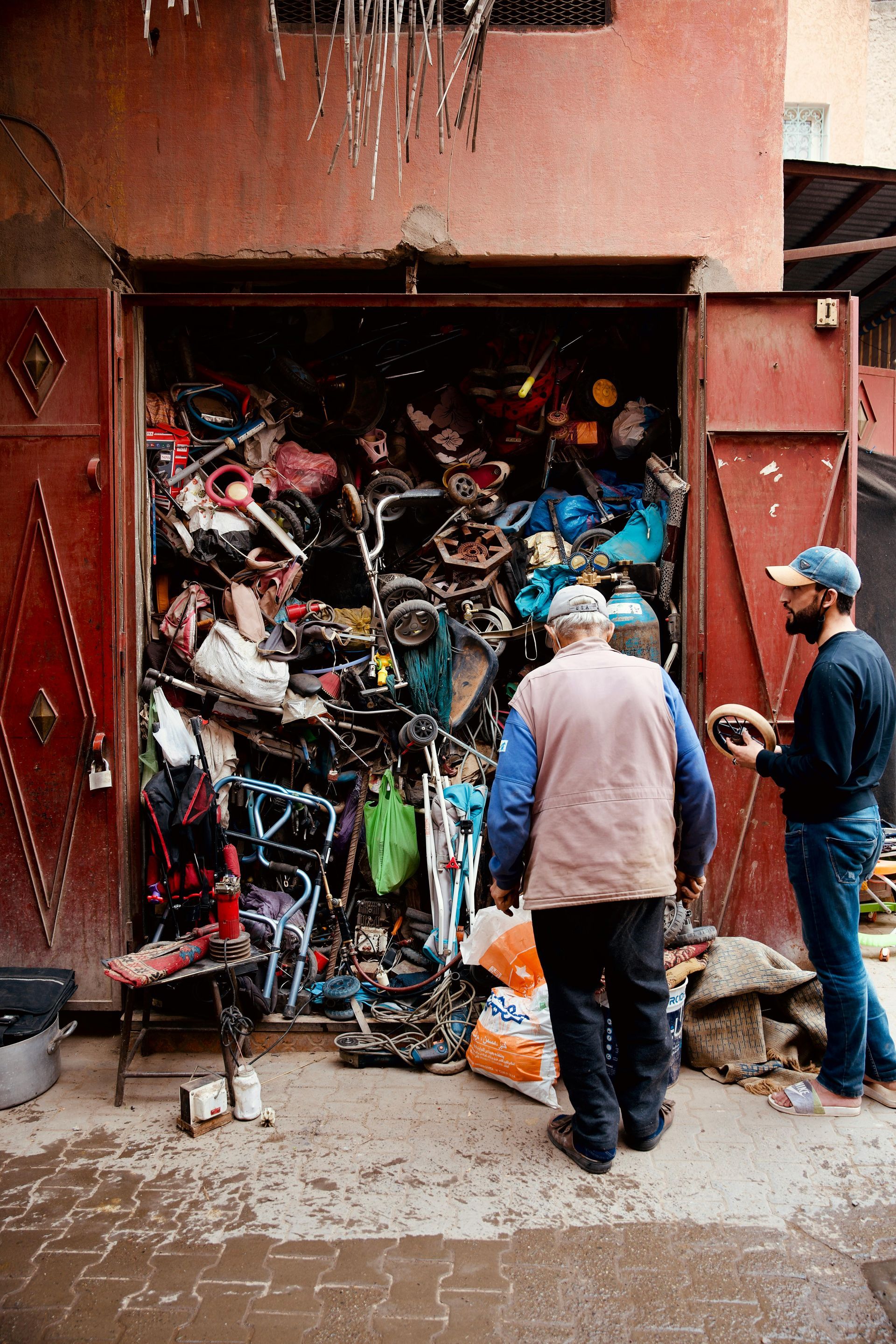 Two men are standing in front of a store filled with lots of items.