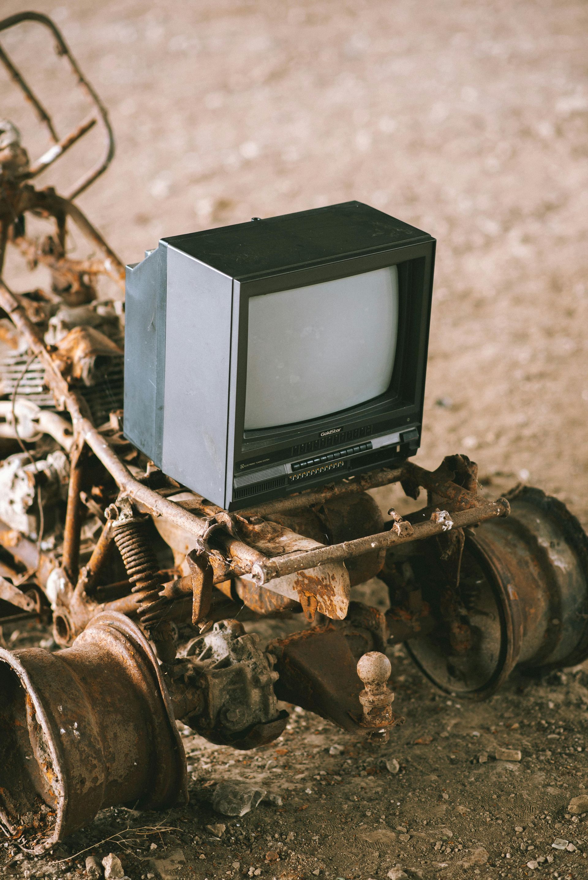 An old television is sitting on top of a rusty vehicle.