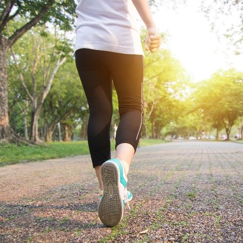 Person walking in a park, wearing athletic clothes, sunny day.