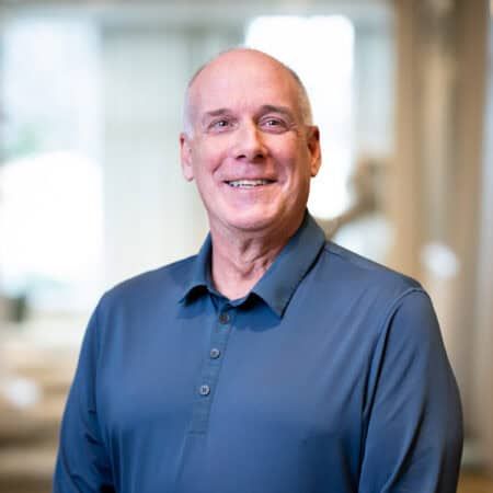 Man in blue polo shirt smiles, blurred background.