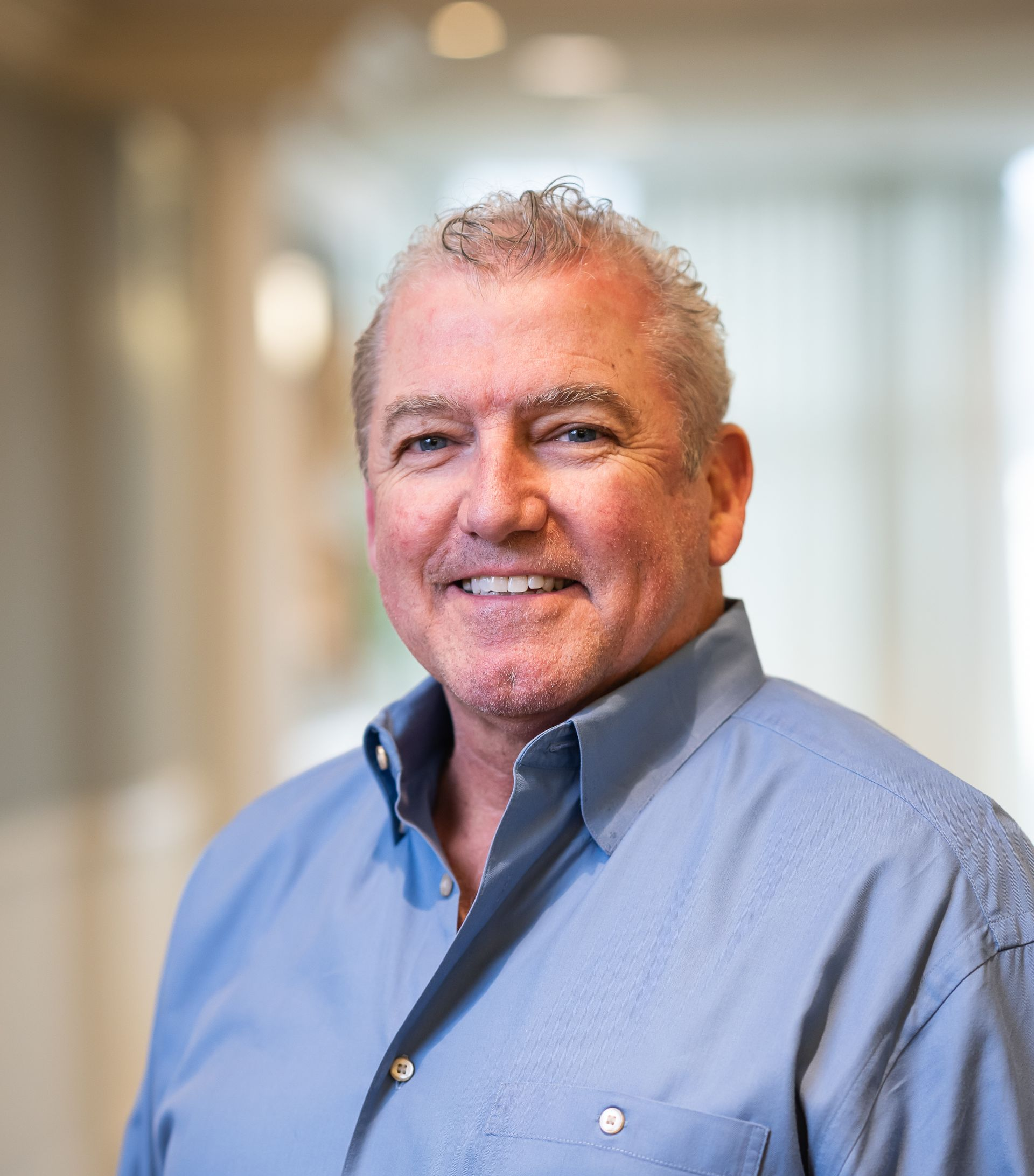 Man in blue shirt smiles, indoors.