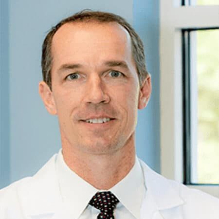 Man in white coat, smiling, in a medical setting.